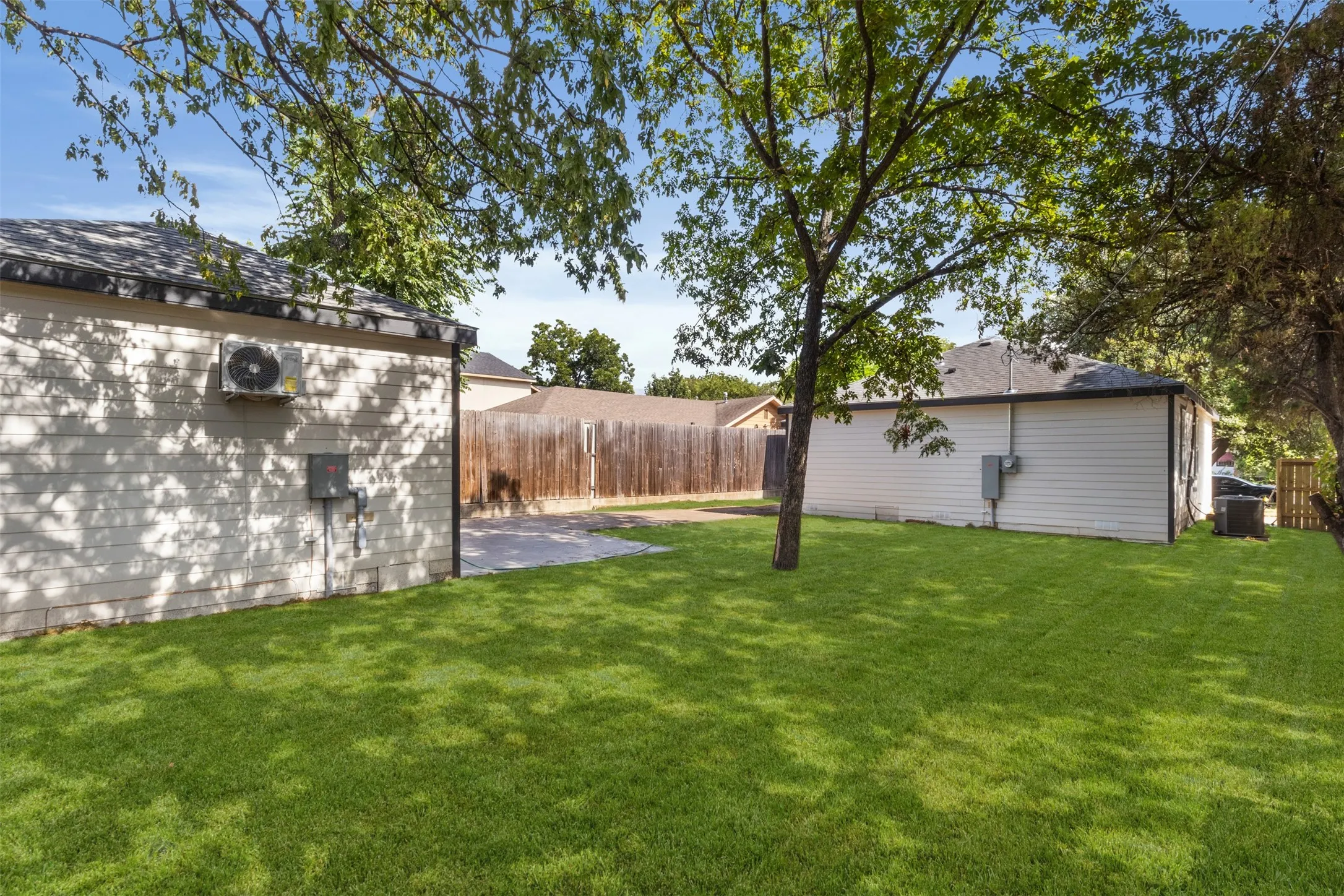 Expansive green lawn, mature trees, wood privacy fencing, and two detached structures with distinct siding
