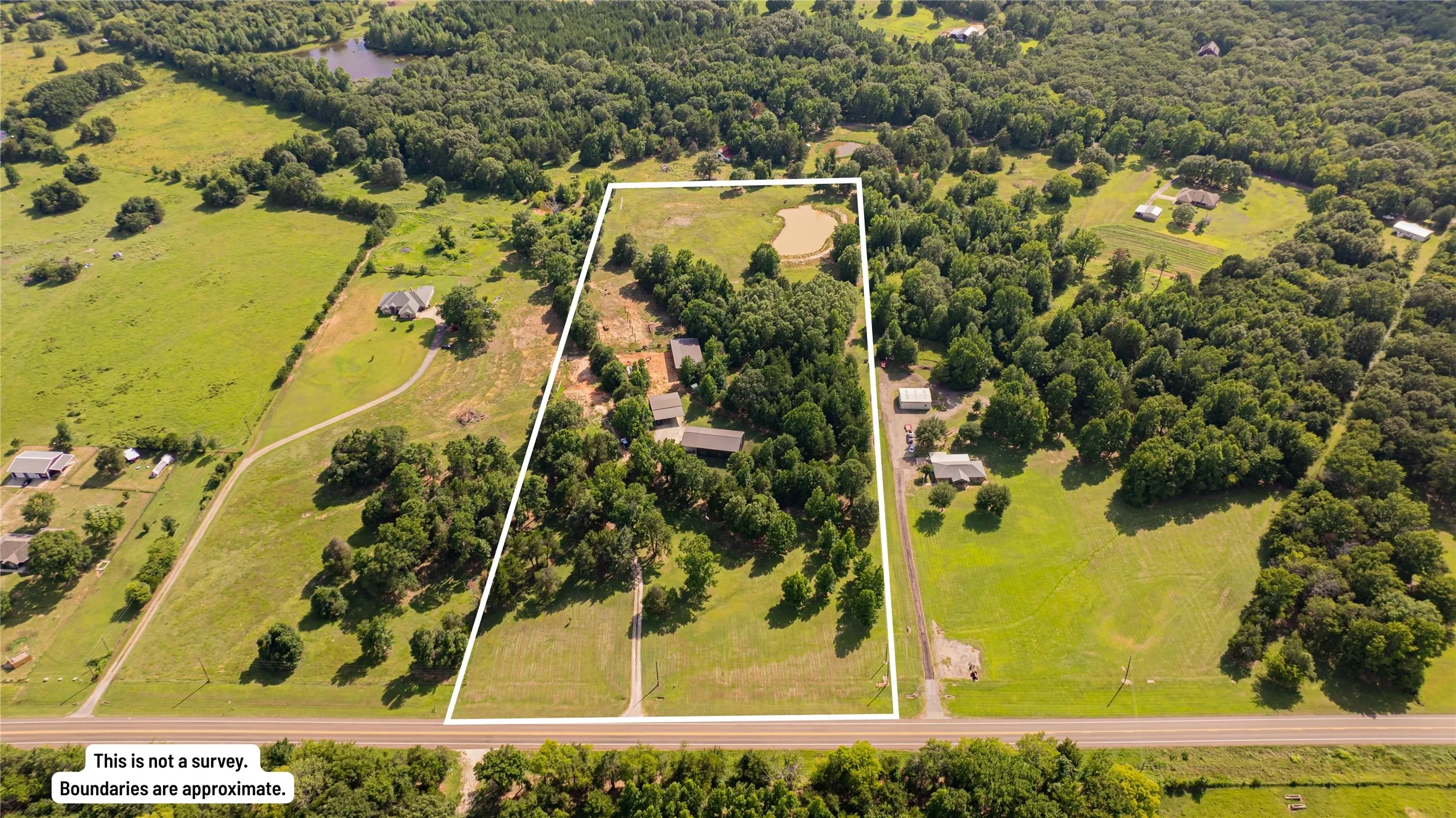 Expansive property featuring a combination of cleared land and mature trees, a natural pond, and multiple structures