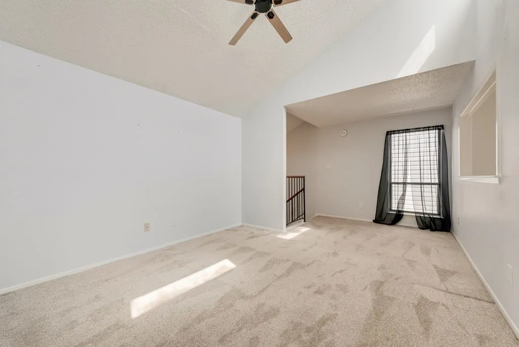 Vaulted ceiling, ceiling fan, carpet flooring, large window, and open railing