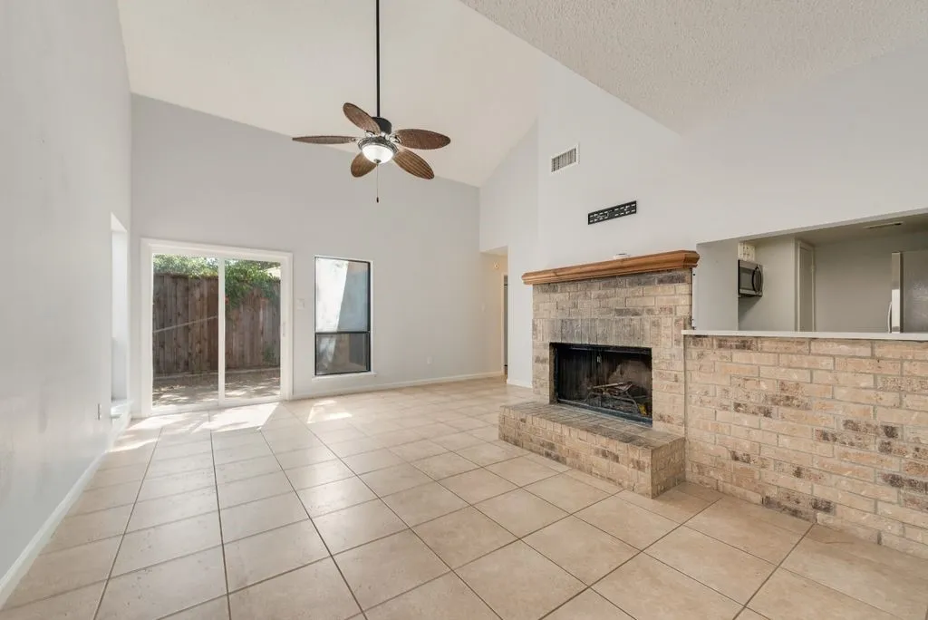 Vaulted ceiling with a ceiling fan, tiled flooring, brick fireplace with a wood mantle, and sliding glass door