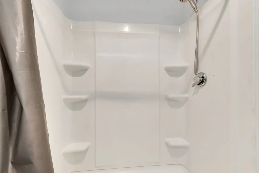 White shower surround with built-in shelving, chrome shower fixture, and handheld showerhead