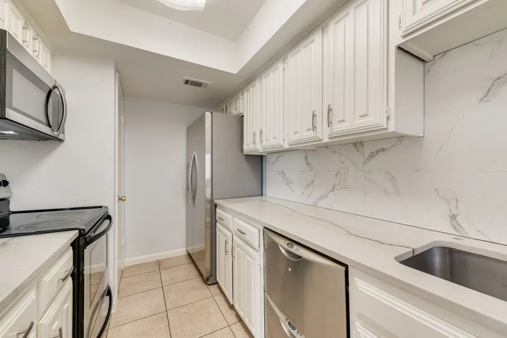 Kitchen featuring white cabinetry, light-toned countertops, a stainless steel microwave, and a stainless steel dishwasher