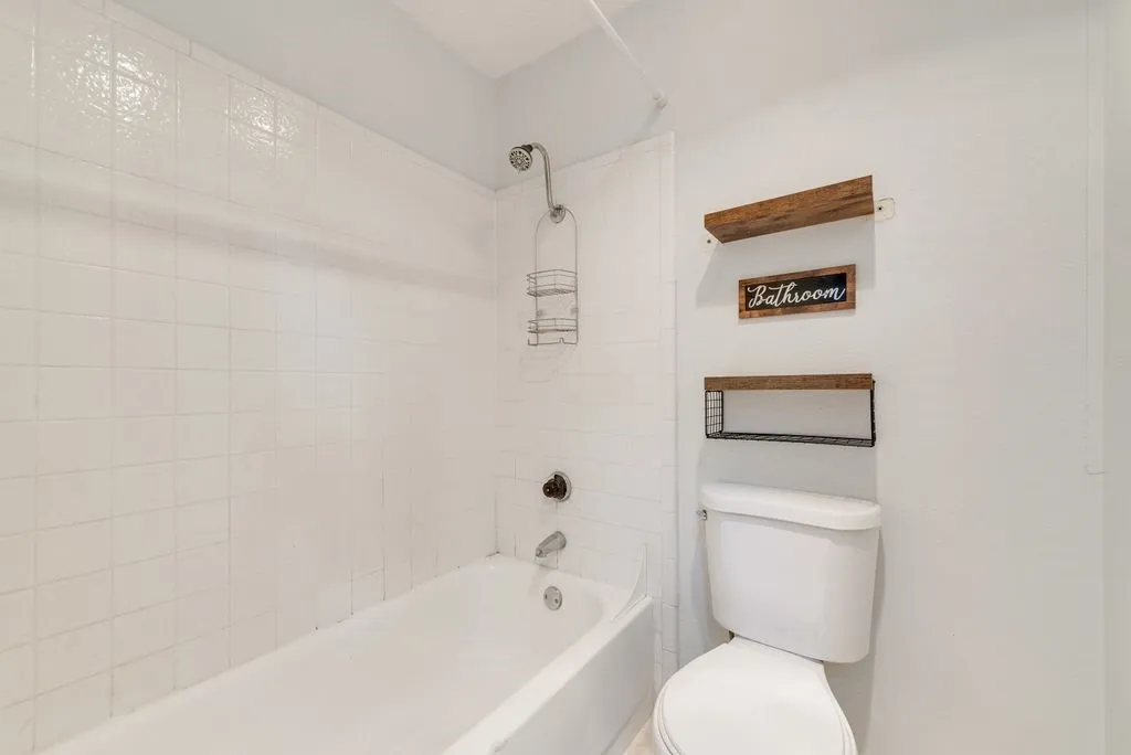 White tile surround shower with a built-in tub, a wall-mounted showerhead, and a white toilet