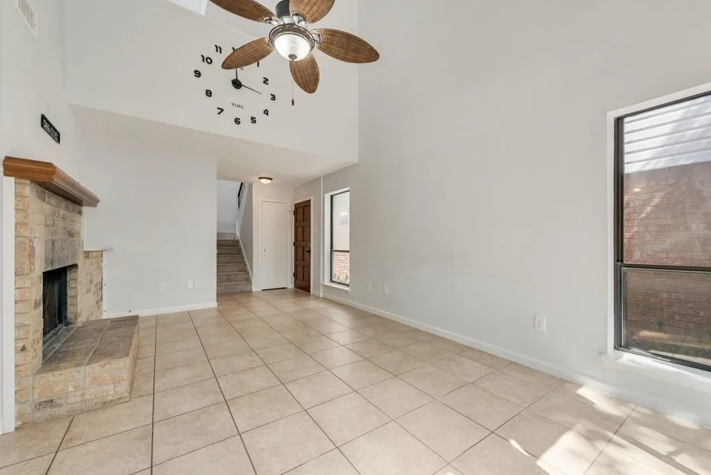 Vaulted ceiling with an attached ceiling fan, stone-clad fireplace with a hearth, tile flooring, and a multi-pane window