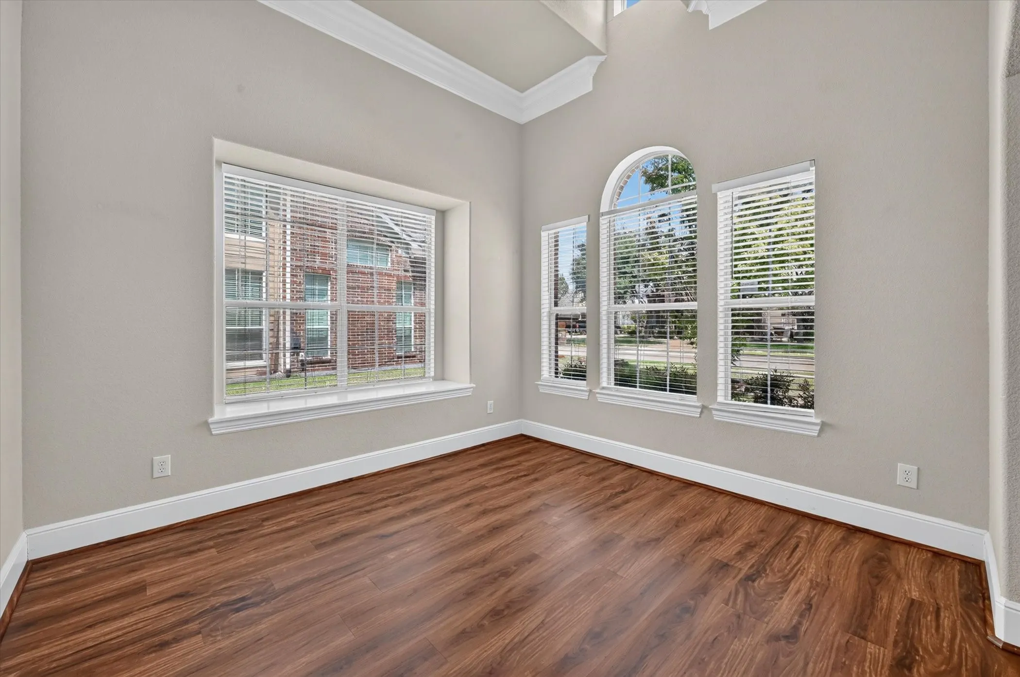 Wood-finish flooring, high ceilings, crown molding, arched window, and multiple windows with blinds