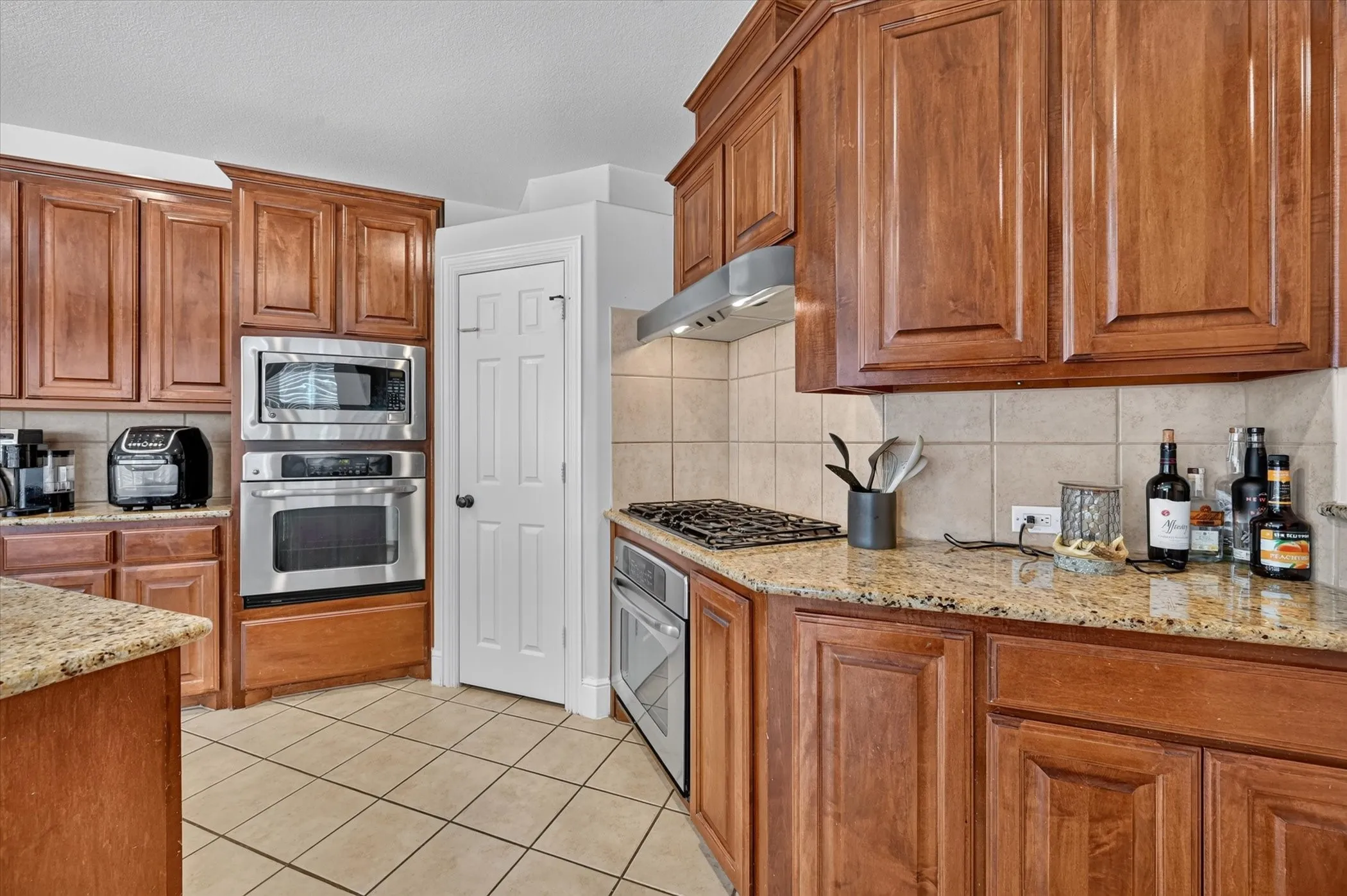 Kitchen featuring extensive wood cabinetry, granite countertops, tile flooring, stainless steel built-in appliances, and a gas cooktop