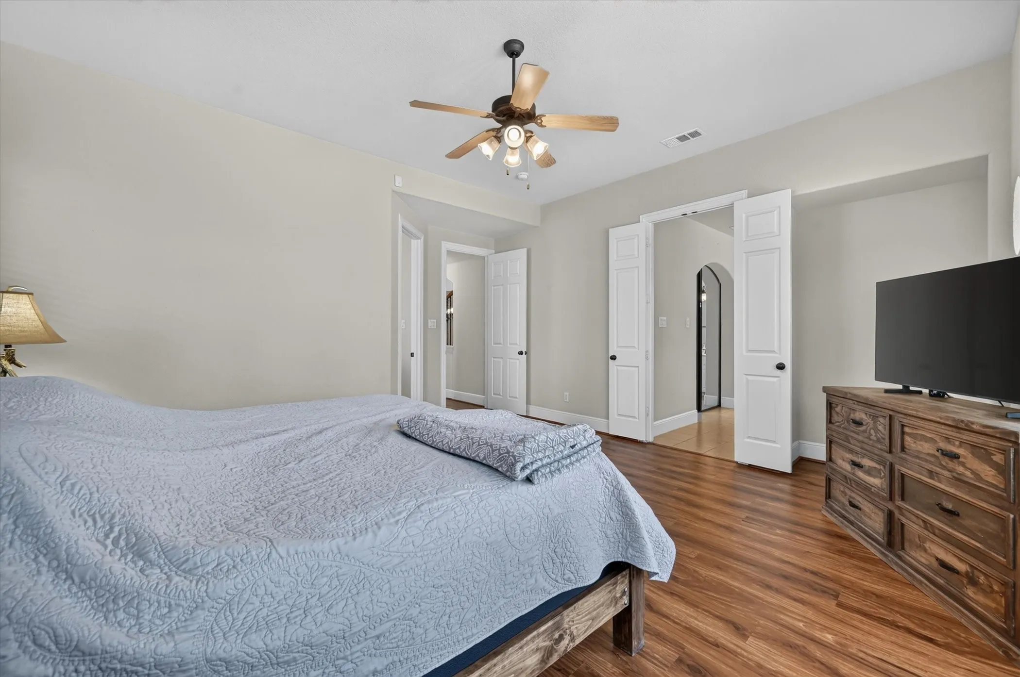 Vaulted ceiling with a ceiling fan, wood-finish flooring, light-toned walls, and white interior doors