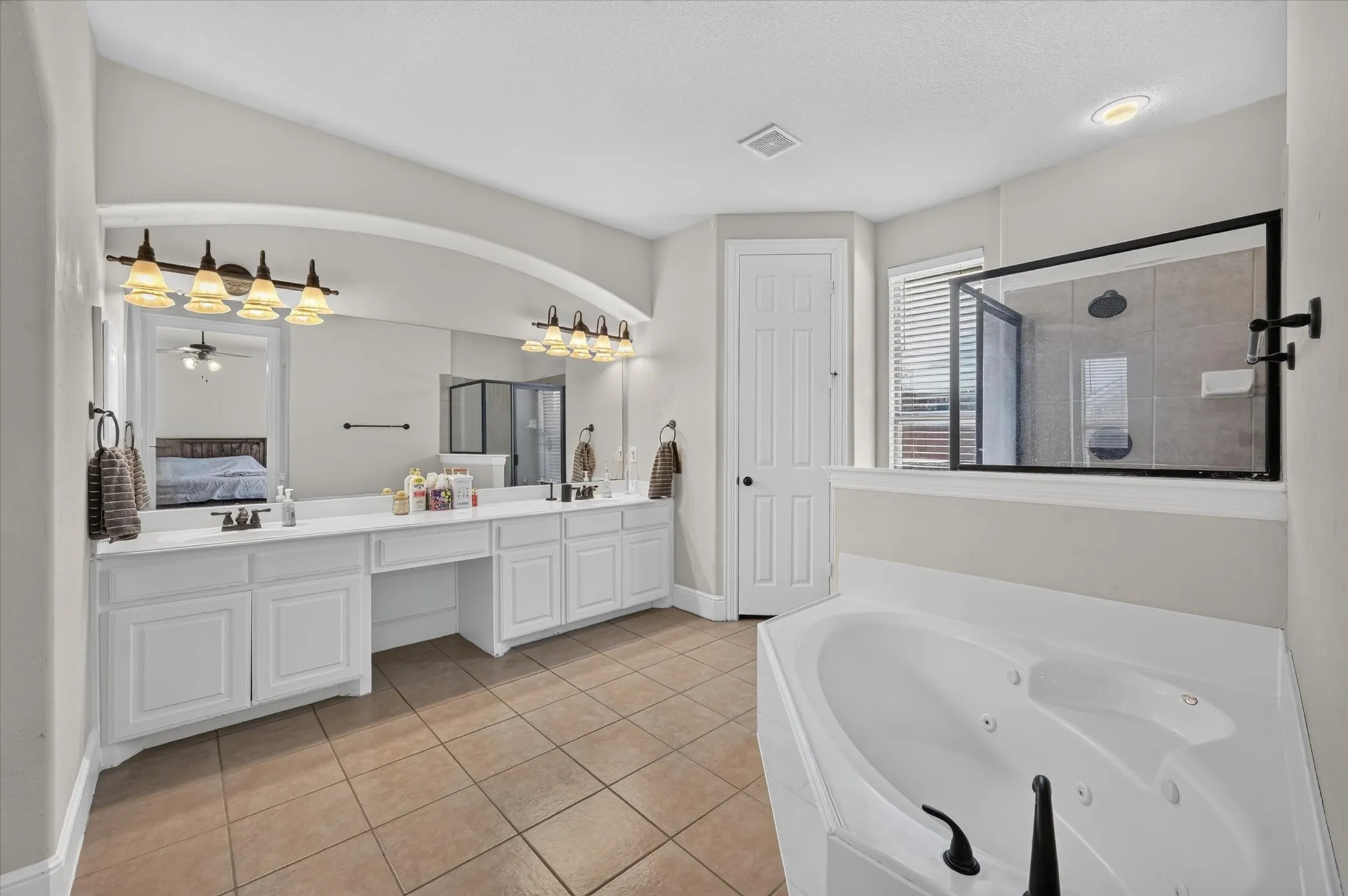 Dual vanity with white cabinetry, built-in makeup vanity, large wall-mounted mirror, and tile flooring