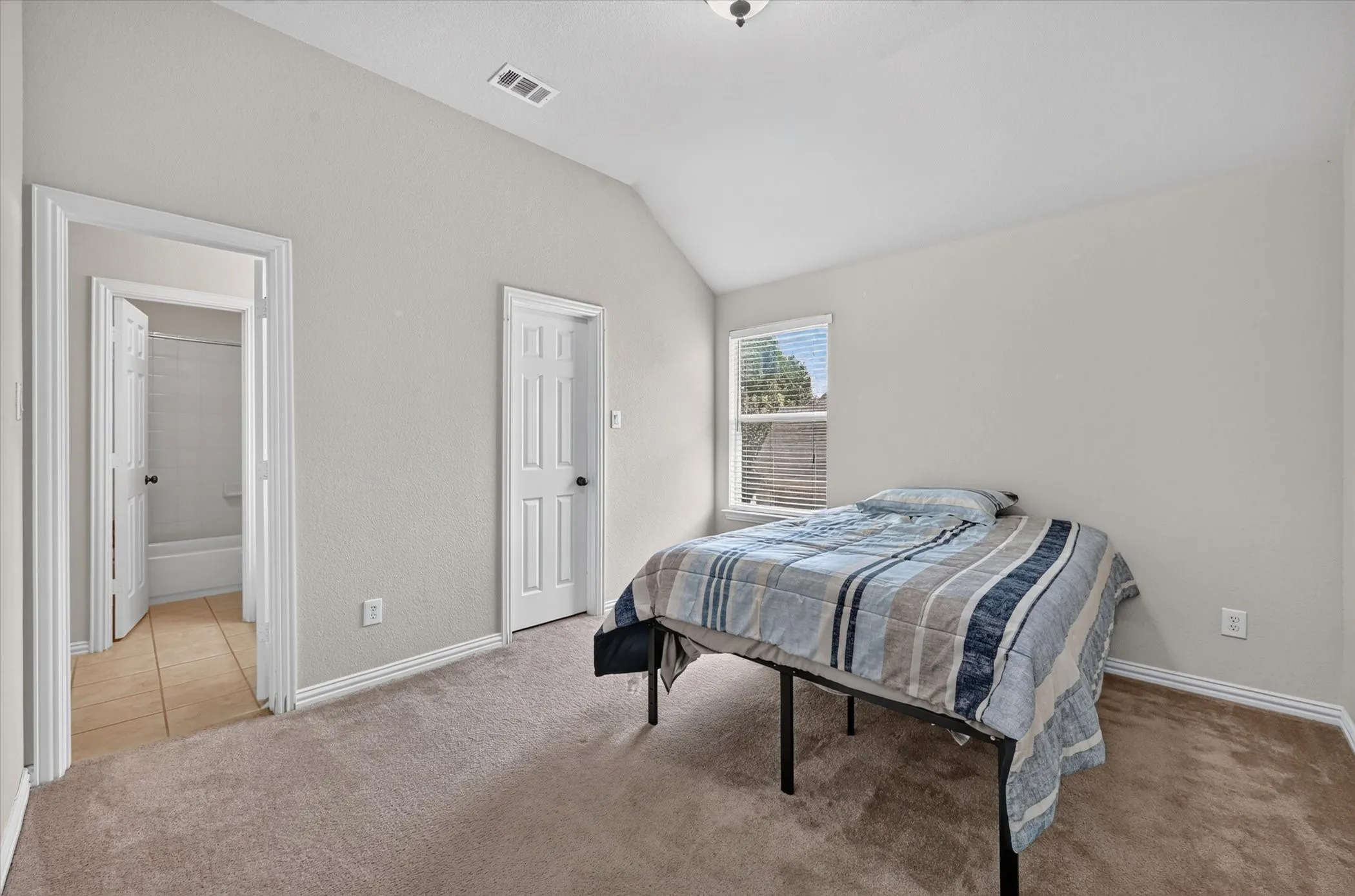 Vaulted ceiling, carpeted flooring, window with blinds, panel doors, and a bathroom with tile flooring and a bathtub