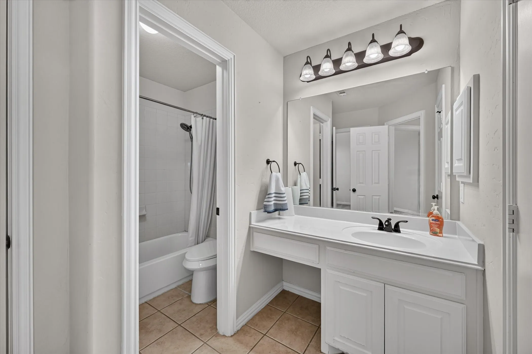 White vanity with an integrated sink and dark-finish faucet, a large wall-mounted mirror, and a five-light fixture