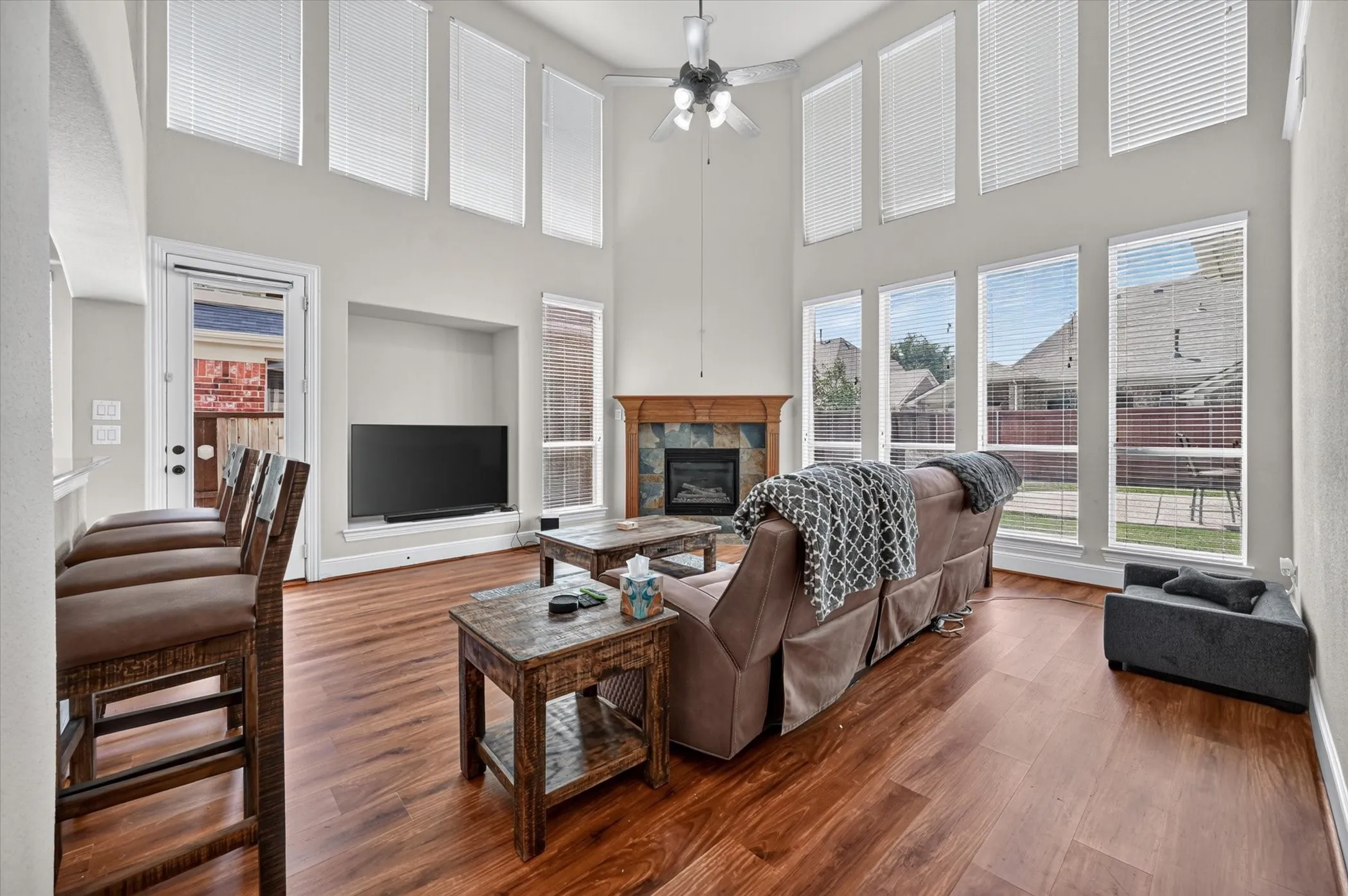 Two-story living area with wood-finish flooring, a stone-surround fireplace, built-in media niche, and multiple windows