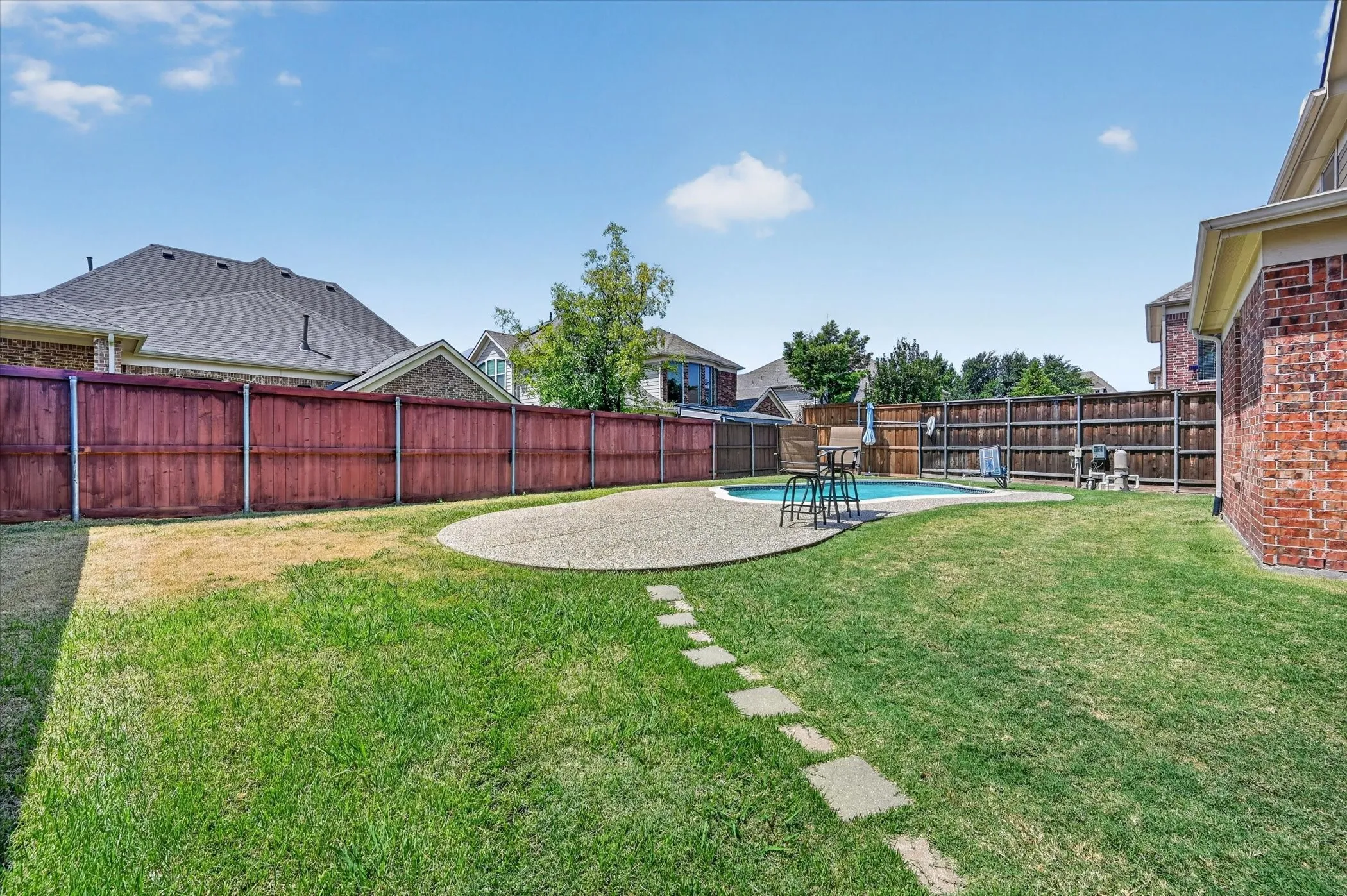 Expansive backyard featuring a swimming pool with an adjacent patio, a stepping stone pathway, and privacy fencing