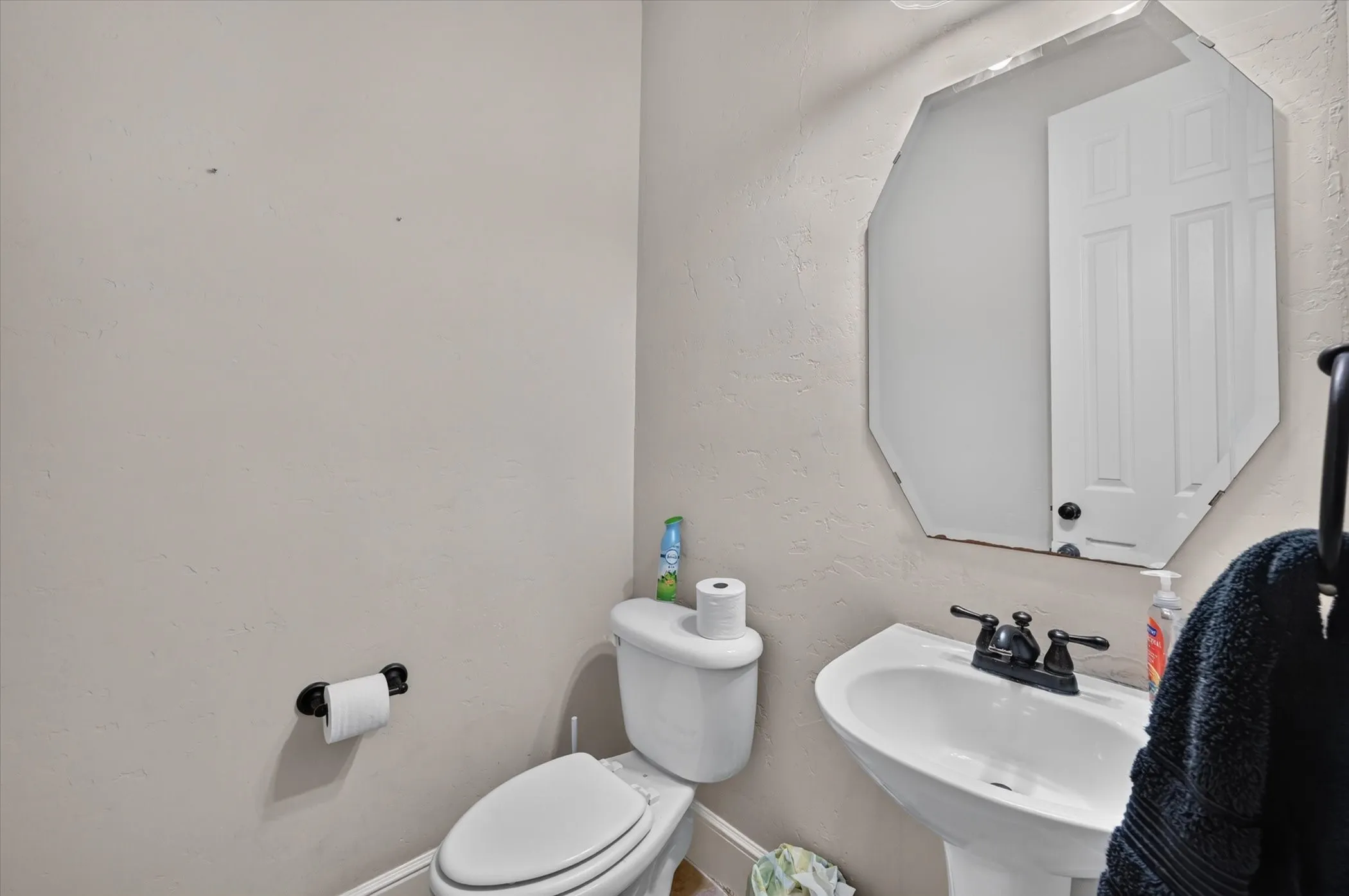 Pedestal sink with dark-finished faucet, rectangular beveled mirror, and textured wall finish