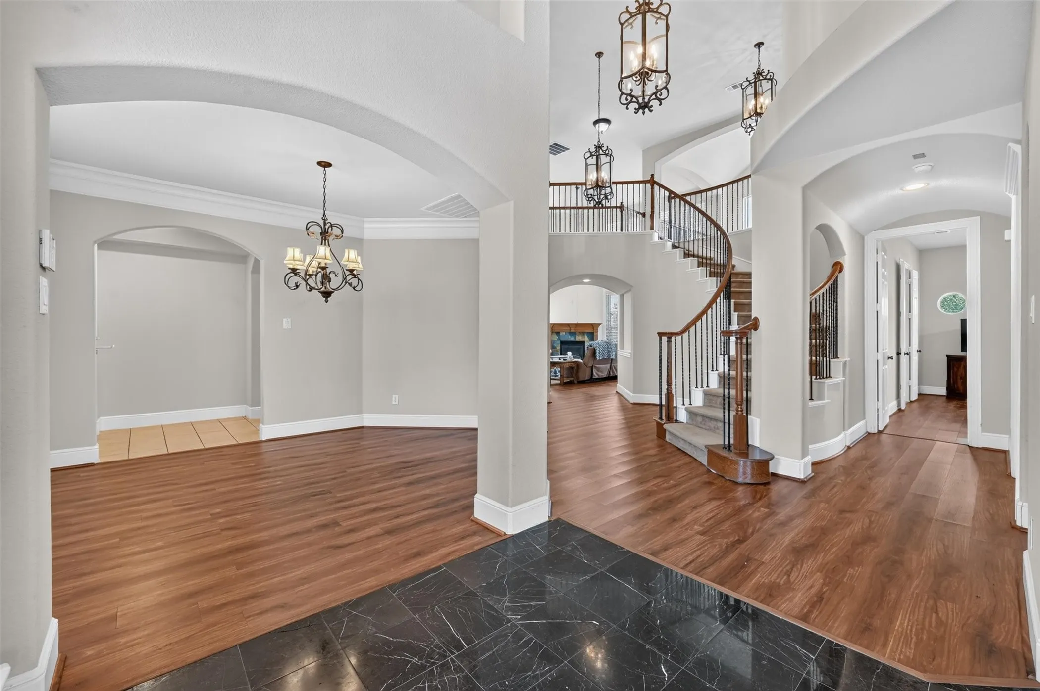 Grand entry with black marble flooring, wood-finish flooring, a winding staircase with dark wood handrails, and elegant chandeliers