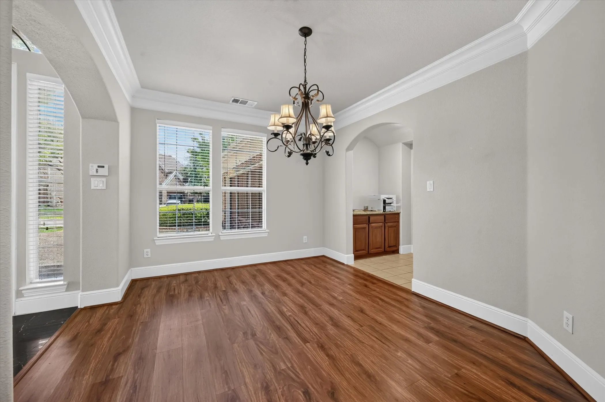 Wood-finish flooring, crown molding, archway, and an ornate chandelier