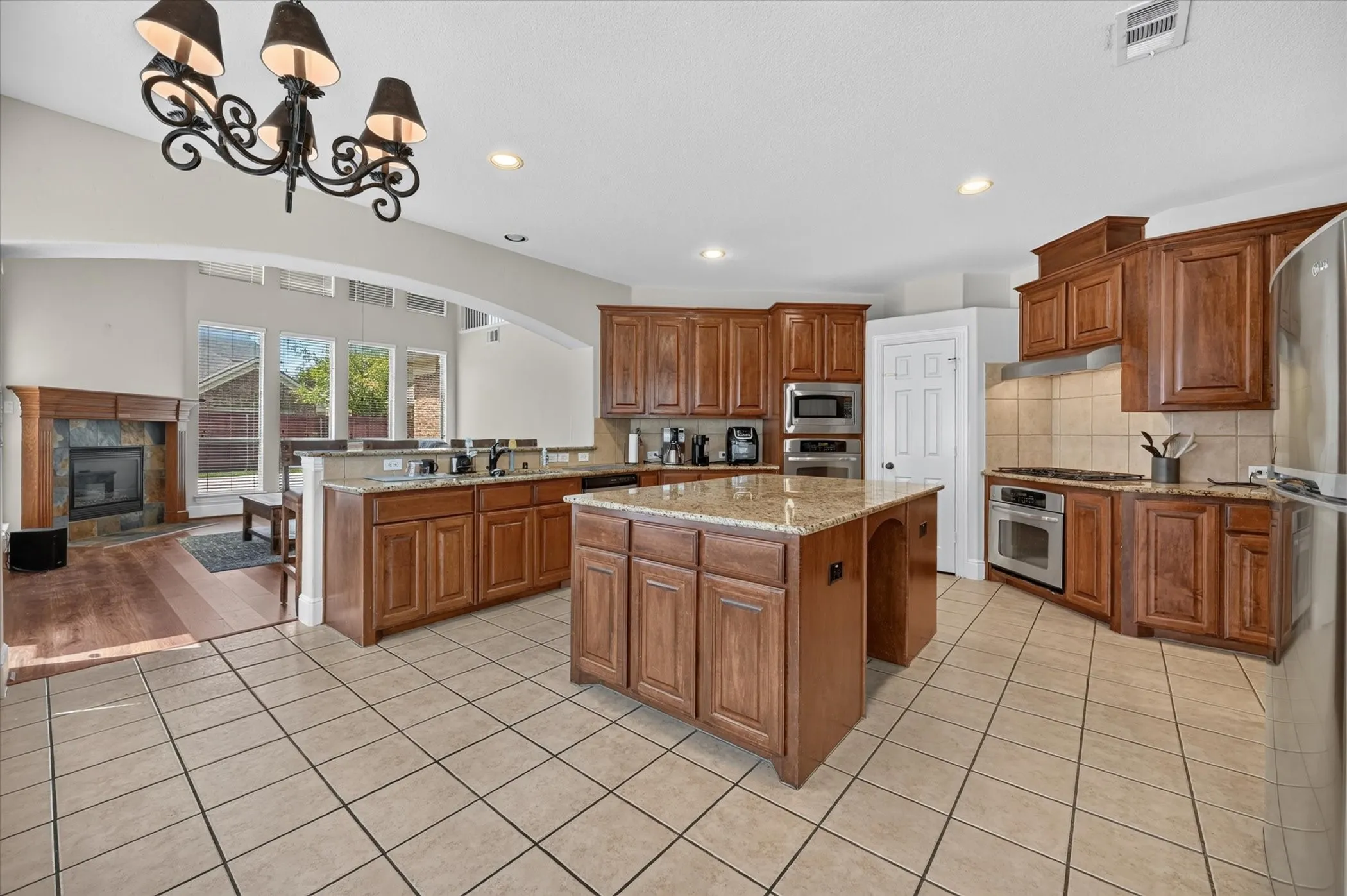 Kitchen featuring wood-finish cabinetry, granite countertops, a central island, stainless steel appliances, and tile flooring