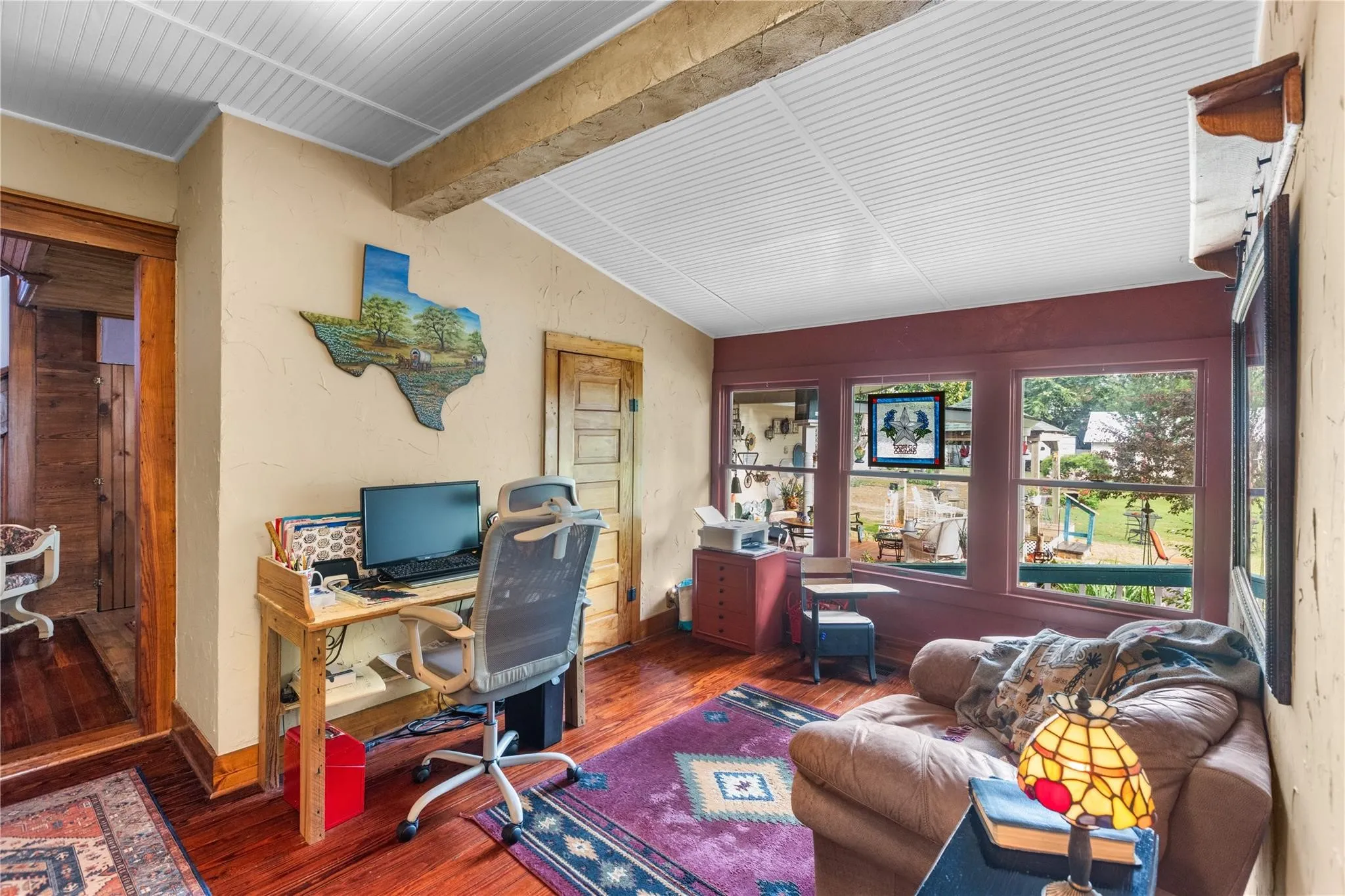 Wood-finish flooring, white beadboard ceiling, exposed wood beam, and multiple windows