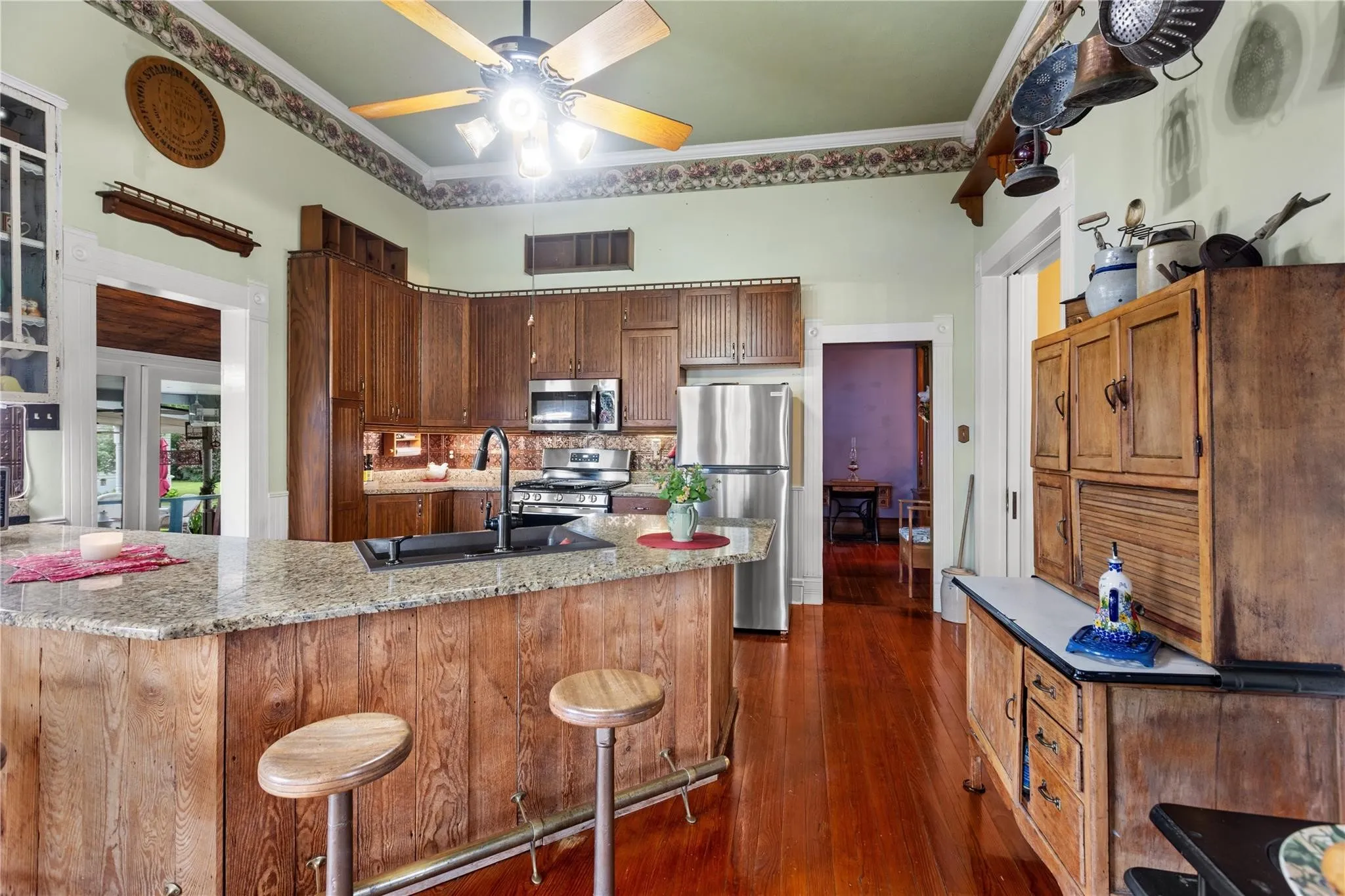Wood-finish flooring throughout, an island with a stone-finish countertop, dark wood cabinetry, and stainless steel appliances