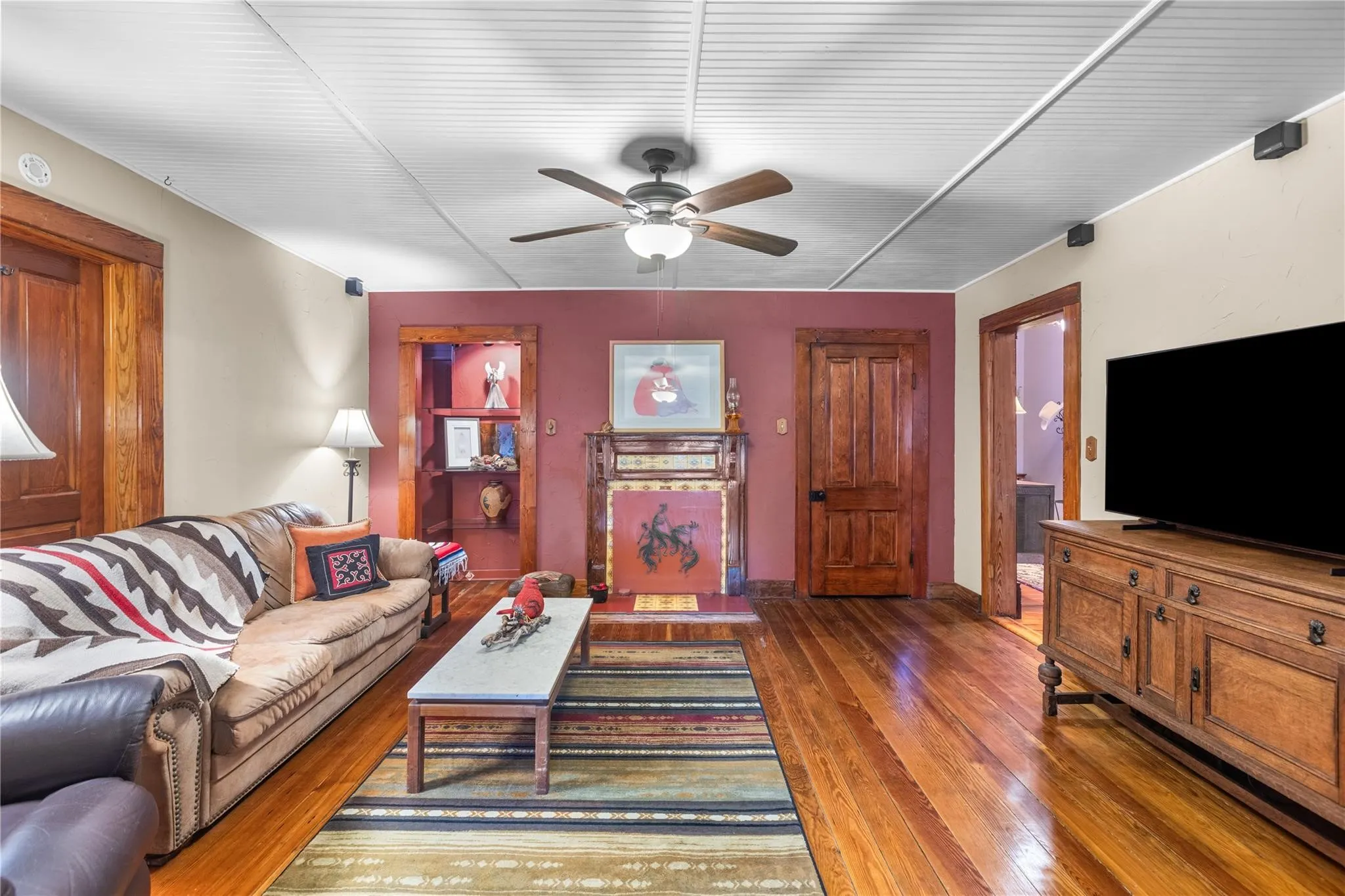 Warm wood-finish flooring with a wood-paneled ceiling, a built-in recessed shelving unit, a ceiling fan, and a fireplace