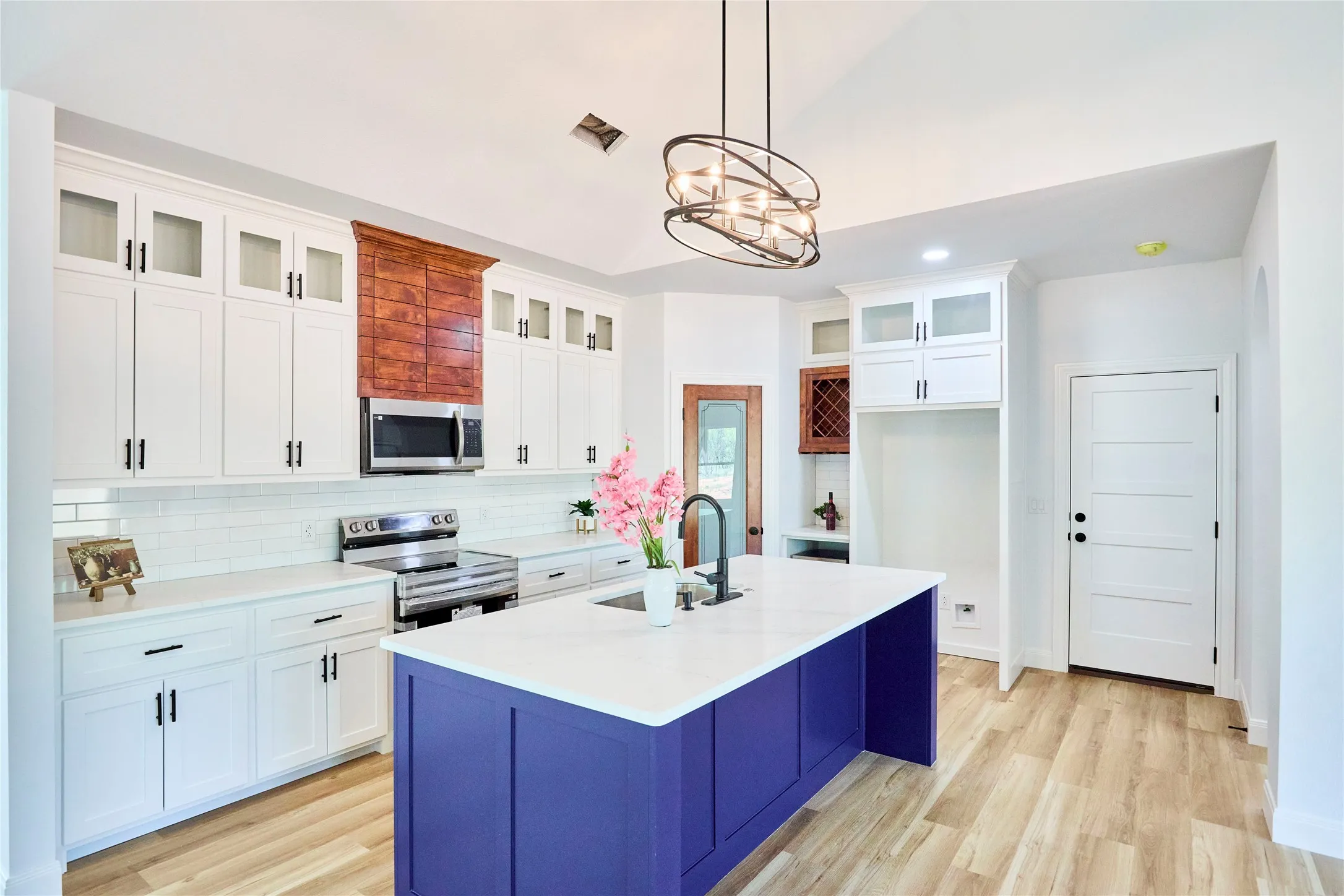 Vaulted ceiling, wood-finish flooring, white cabinetry with black hardware, stainless steel range and microwave, and a central island with a solid surface countertop