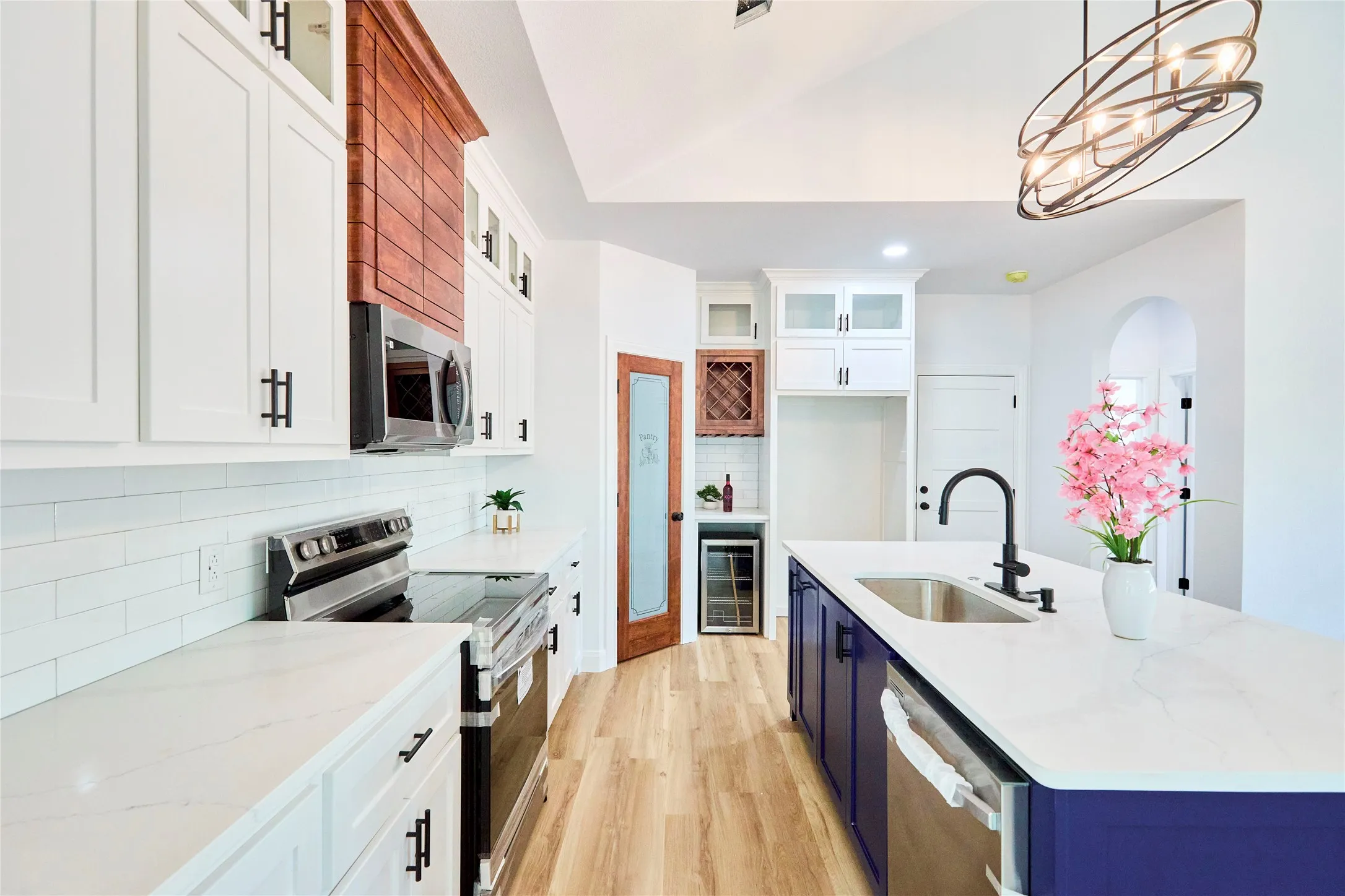 Kitchen featuring white cabinetry, a built-in microwave, wood-finish flooring, a central island with an integrated sink, and an arched doorway