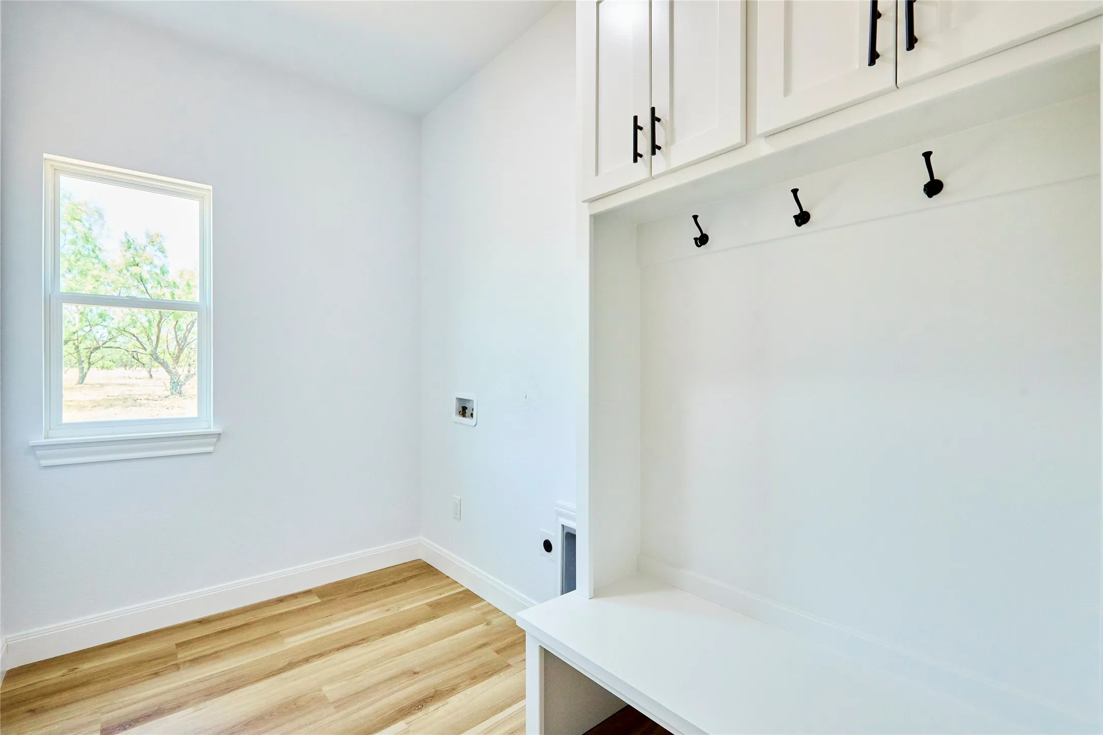 Wood-finish flooring, built-in storage with shaker-style cabinetry, matte black hardware, integrated bench seating, and a window