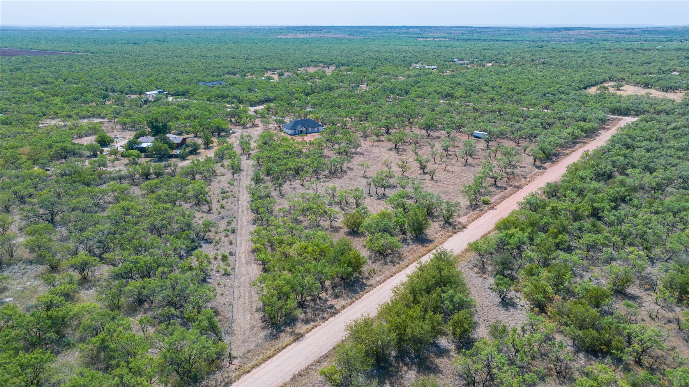 Expansive natural landscape featuring a single-family residence, mature trees, and a dirt road