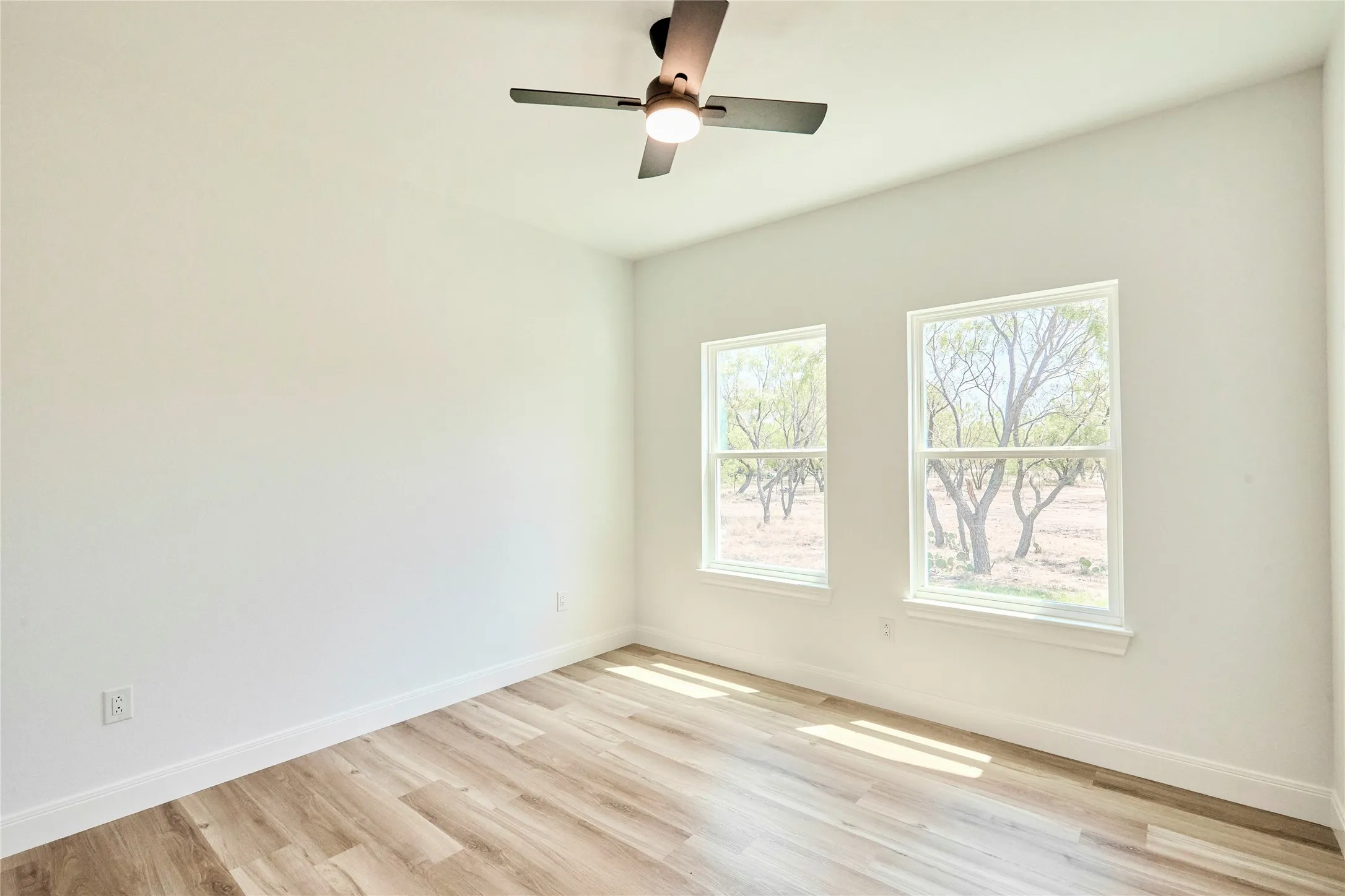 Wood-finish flooring, white walls, two double-hung windows, and a ceiling fan with integrated lighting