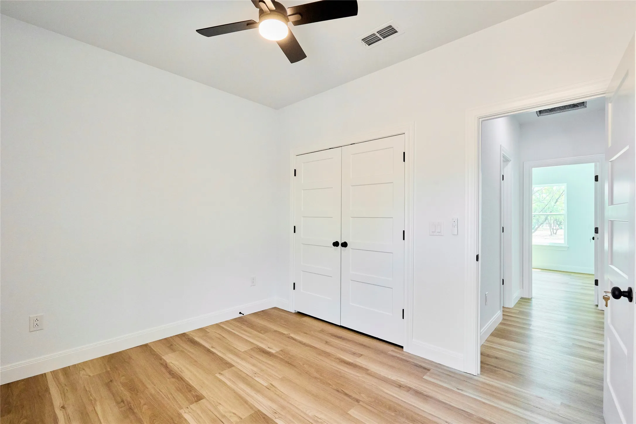Wood-finish flooring, white walls, and a ceiling fan with integrated lighting