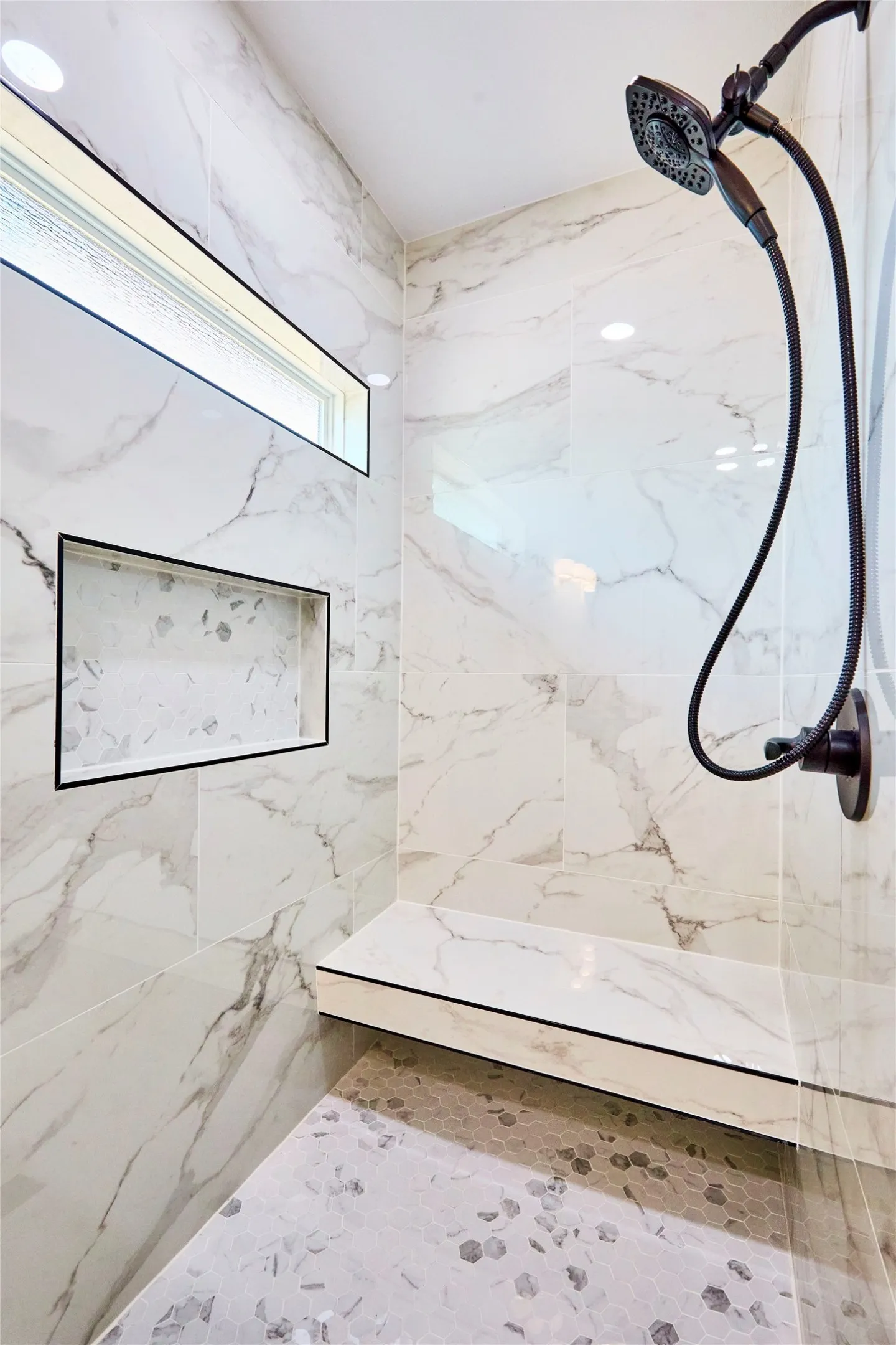 Shower featuring white marble-look wall tiling, a built-in bench, a recessed niche, a horizontal recessed window, and oil-rubbed bronze shower fixtures
