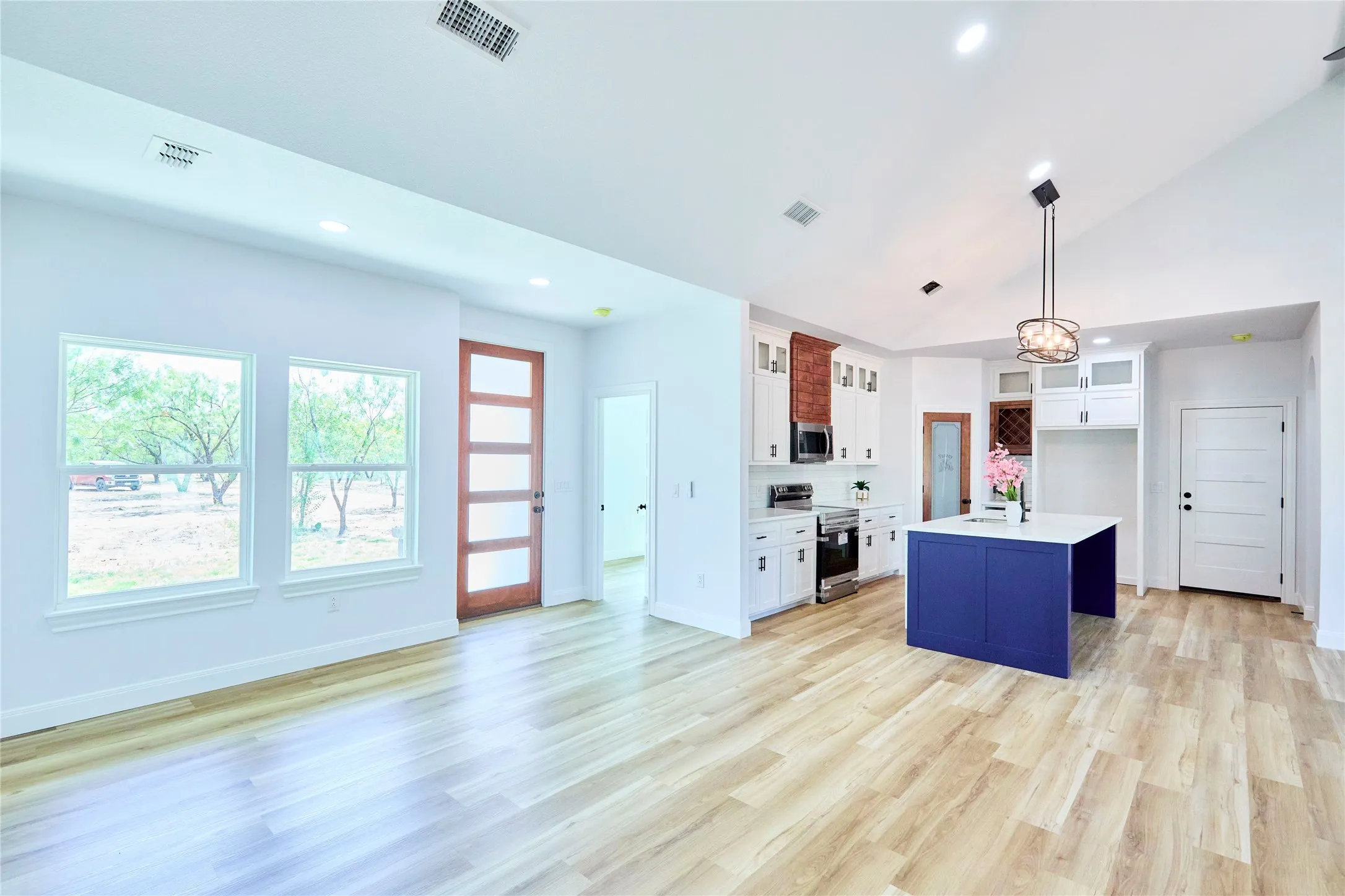 Vaulted ceiling, recessed lighting, wood-finish flooring, white cabinetry, and a kitchen island with a white countertop