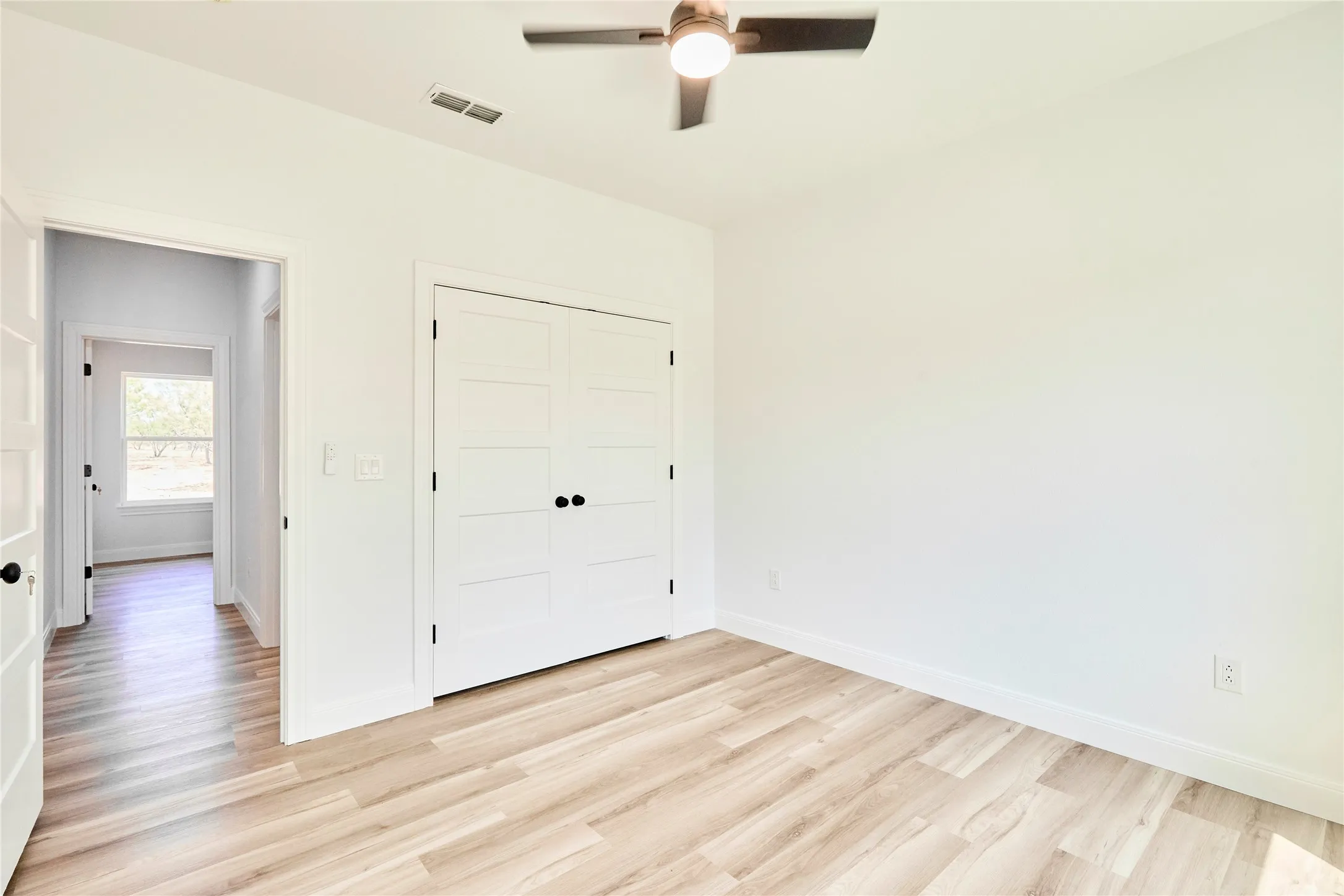 Wood-finish flooring, white walls, and a ceiling fan with integrated lighting