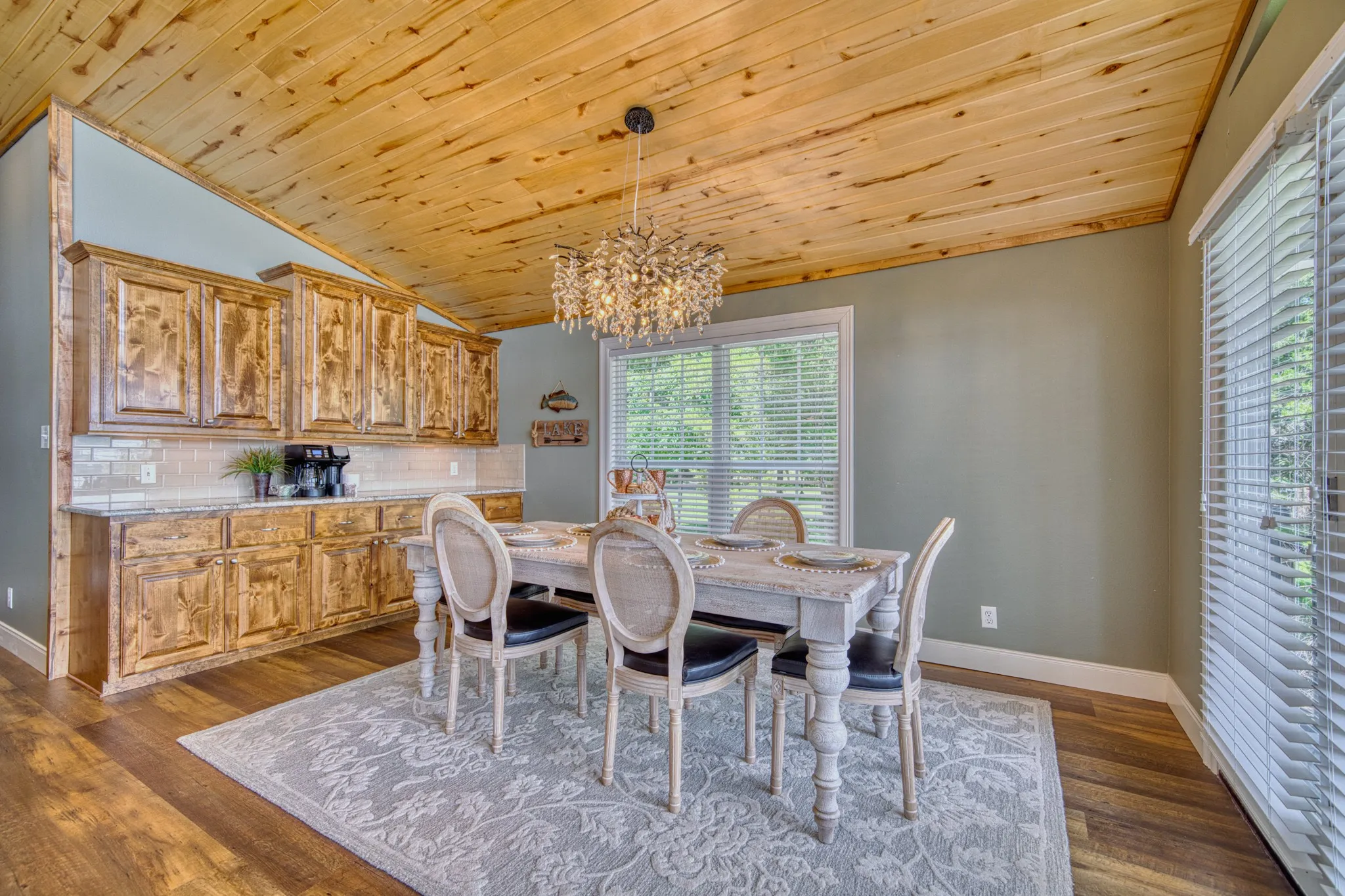 Vaulted wood-plank ceiling, wood-finish flooring, custom wood cabinetry, subway tile backsplash, and a contemporary chandelier