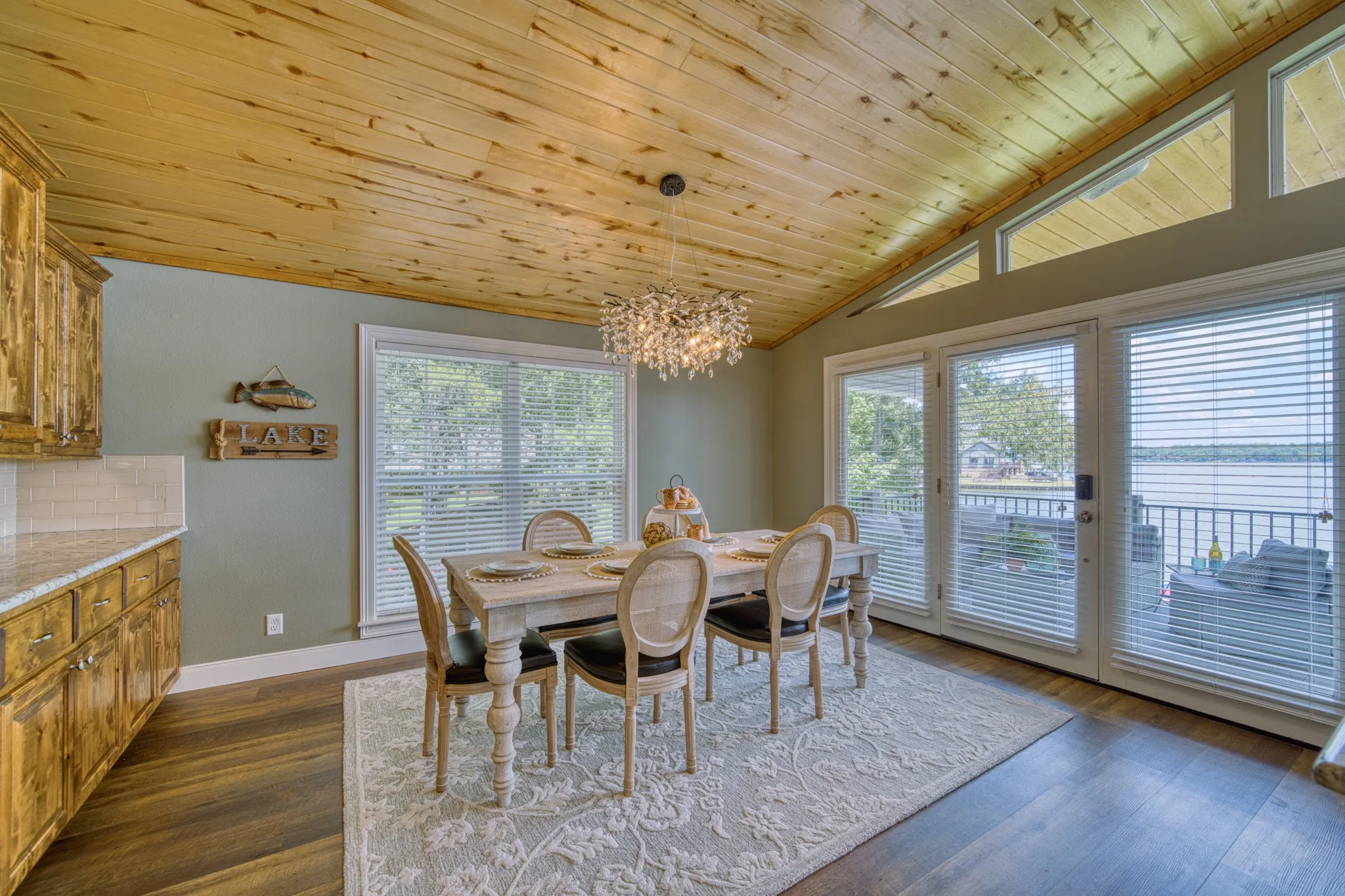 Vaulted wood-paneled ceiling, wood-finish flooring, built-in cabinetry with light-toned countertops and subway tile backsplash, and expansive glass doors opening to a balcony with water scenery