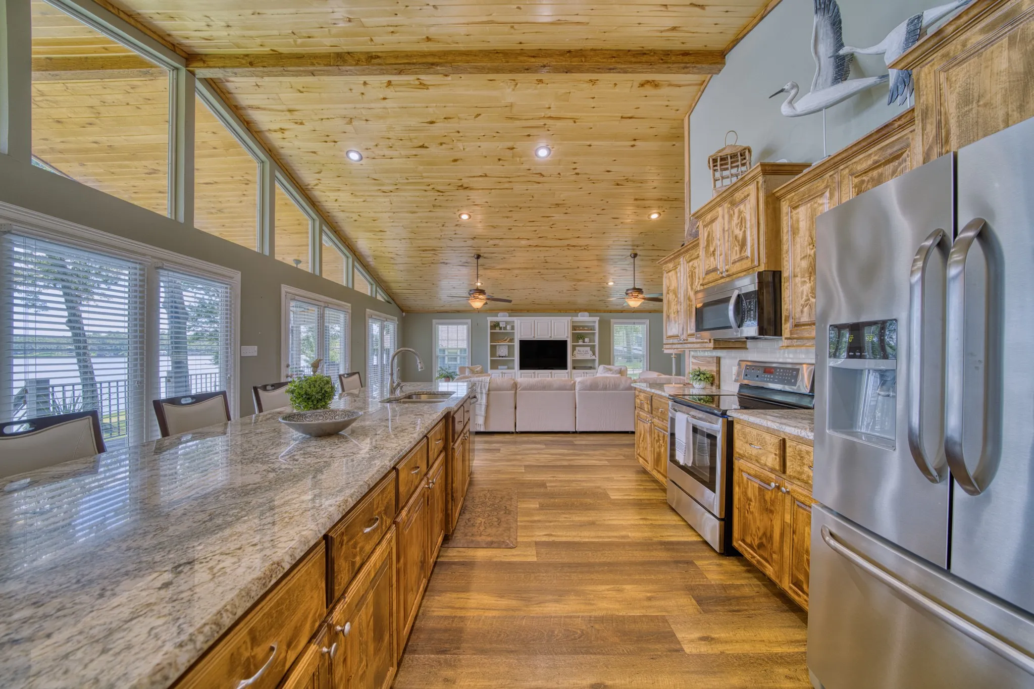 Spacious kitchen featuring an extended island with stone countertop, stainless steel appliances, custom wood cabinetry, and wood-finish flooring