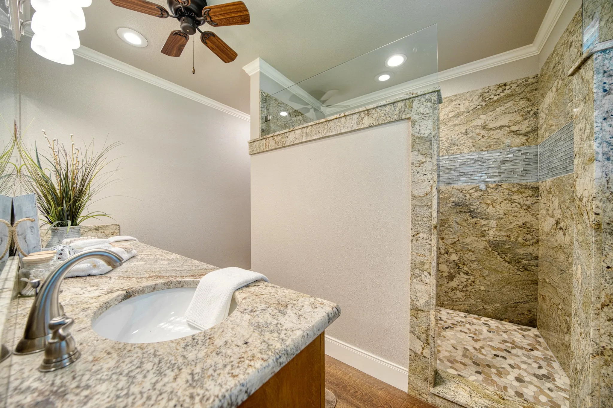 Walk-in shower with natural stone tile surround, mosaic accent band, and river rock flooring