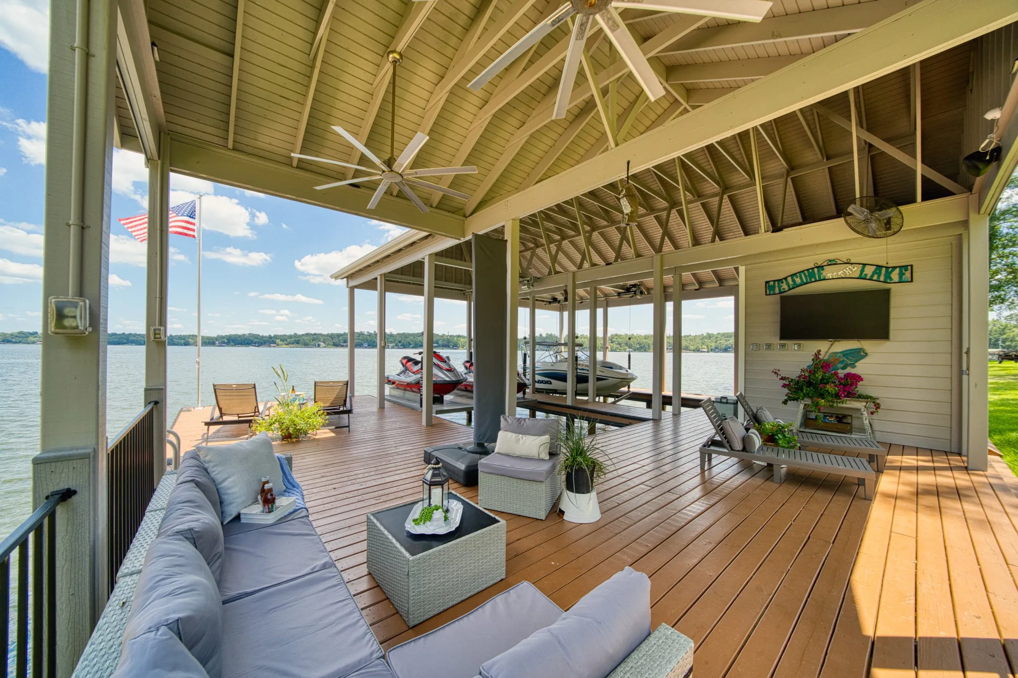 Expansive covered deck featuring a vaulted ceiling with multiple ceiling fans, wood-finish decking, and direct water access with boat slips