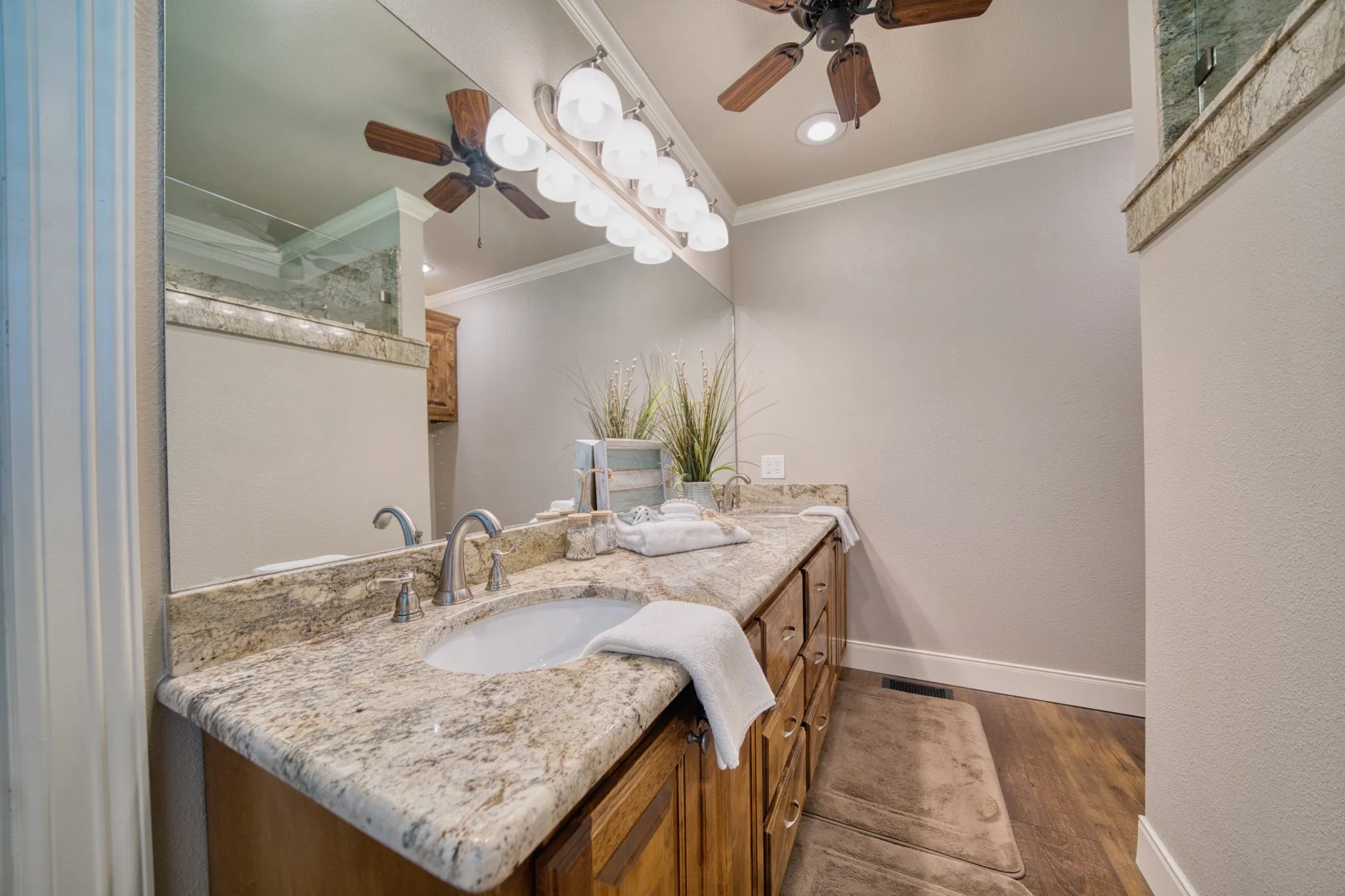 Expansive vanity with a stone countertop, dual undermount sinks, wood-finish cabinetry, and a ceiling fan