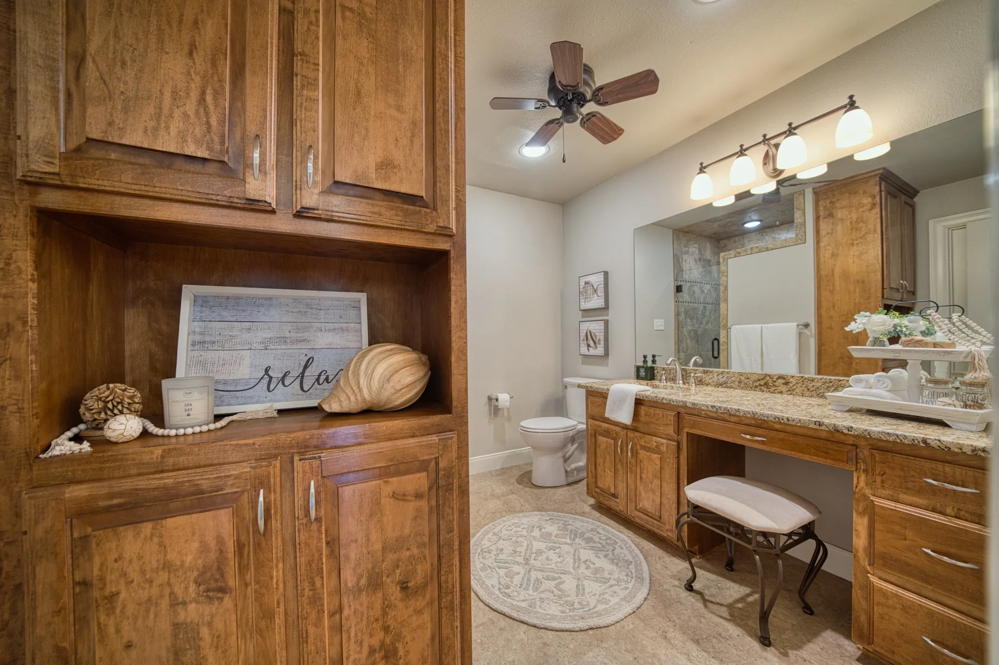 Built-in wood cabinetry, dual vanity with granite-style countertop, large vanity mirror, ceiling fan, and recessed lighting