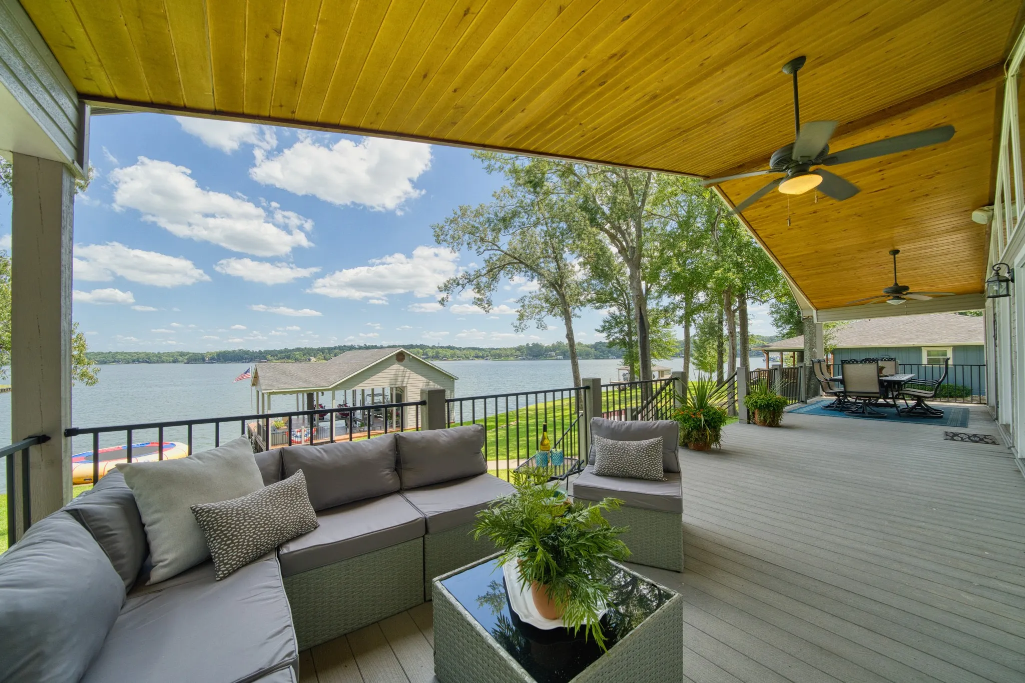 Expansive covered porch featuring a wood-panel ceiling, multiple ceiling fans, and composite decking