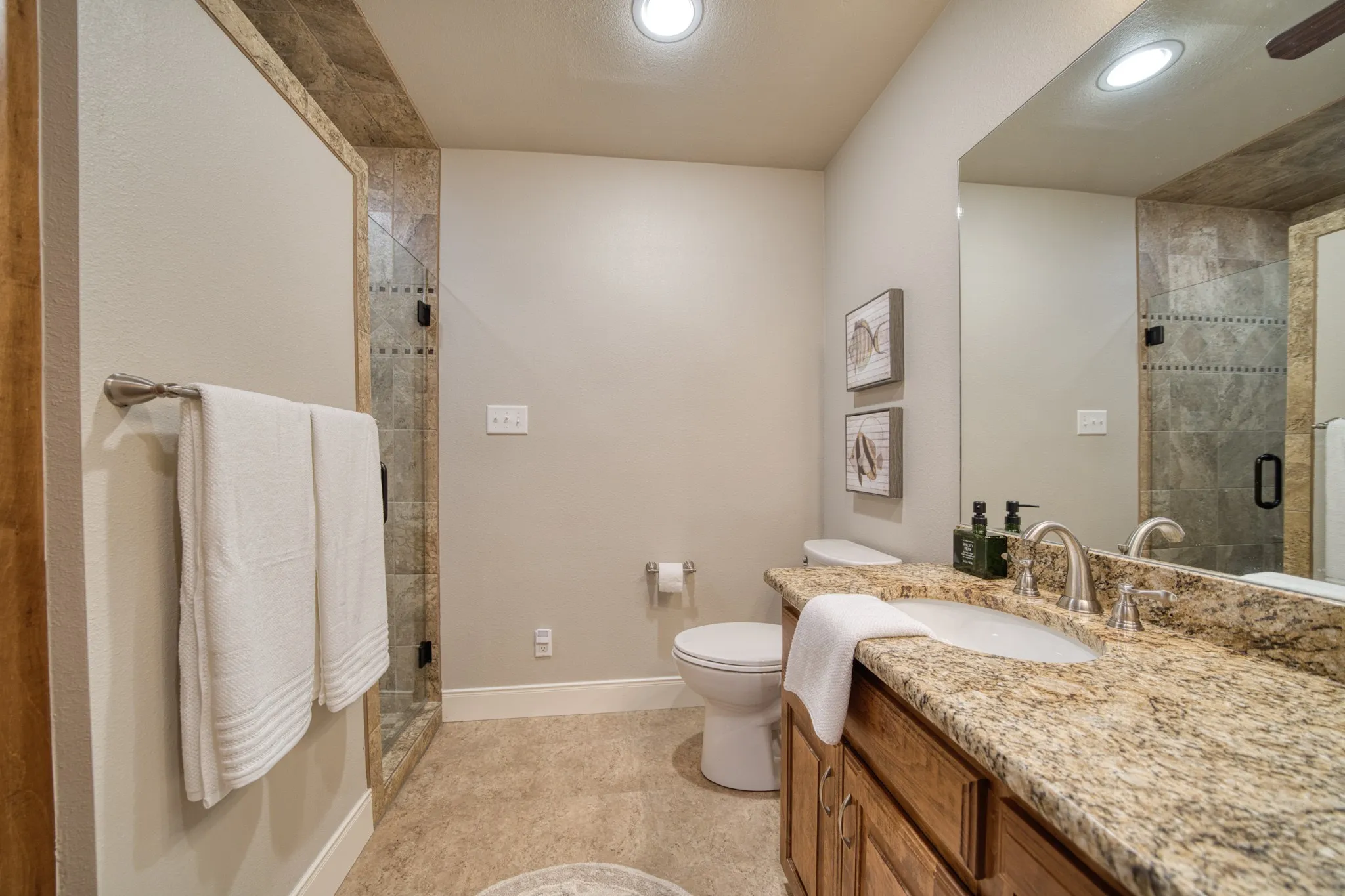 Bathroom featuring a granite-style countertop, wood-finish vanity, undermount sink, and a tiled shower with glass enclosure