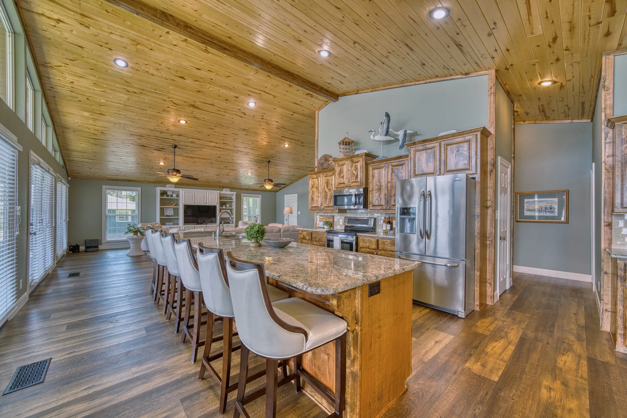 Kitchen with granite-topped island, stainless steel appliances, wood-finish flooring, and a wood-paneled vaulted ceiling with recessed lighting