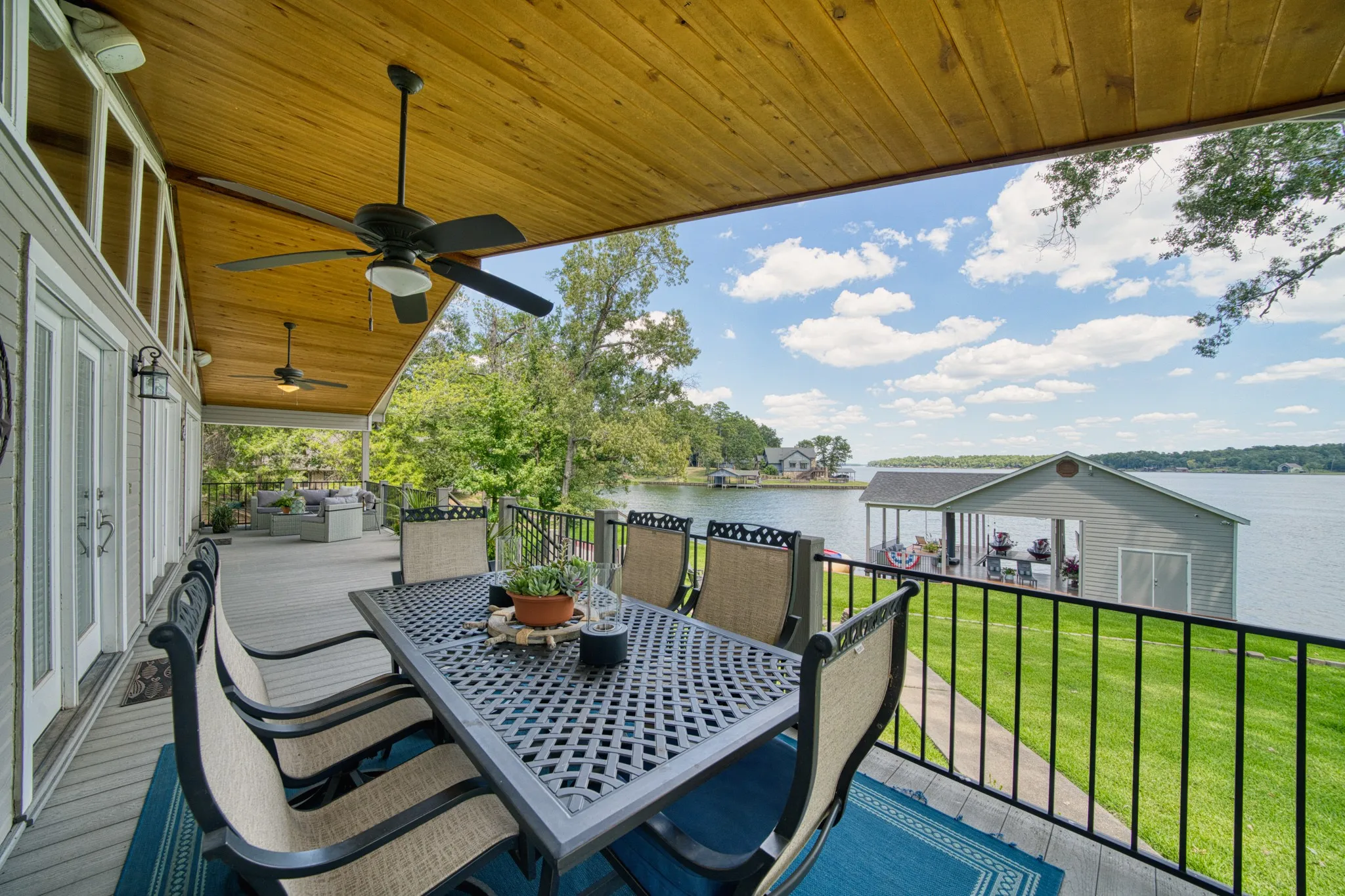 Covered deck featuring a wood-finish ceiling, multiple ceiling fans, and a black railing overlooking a lake