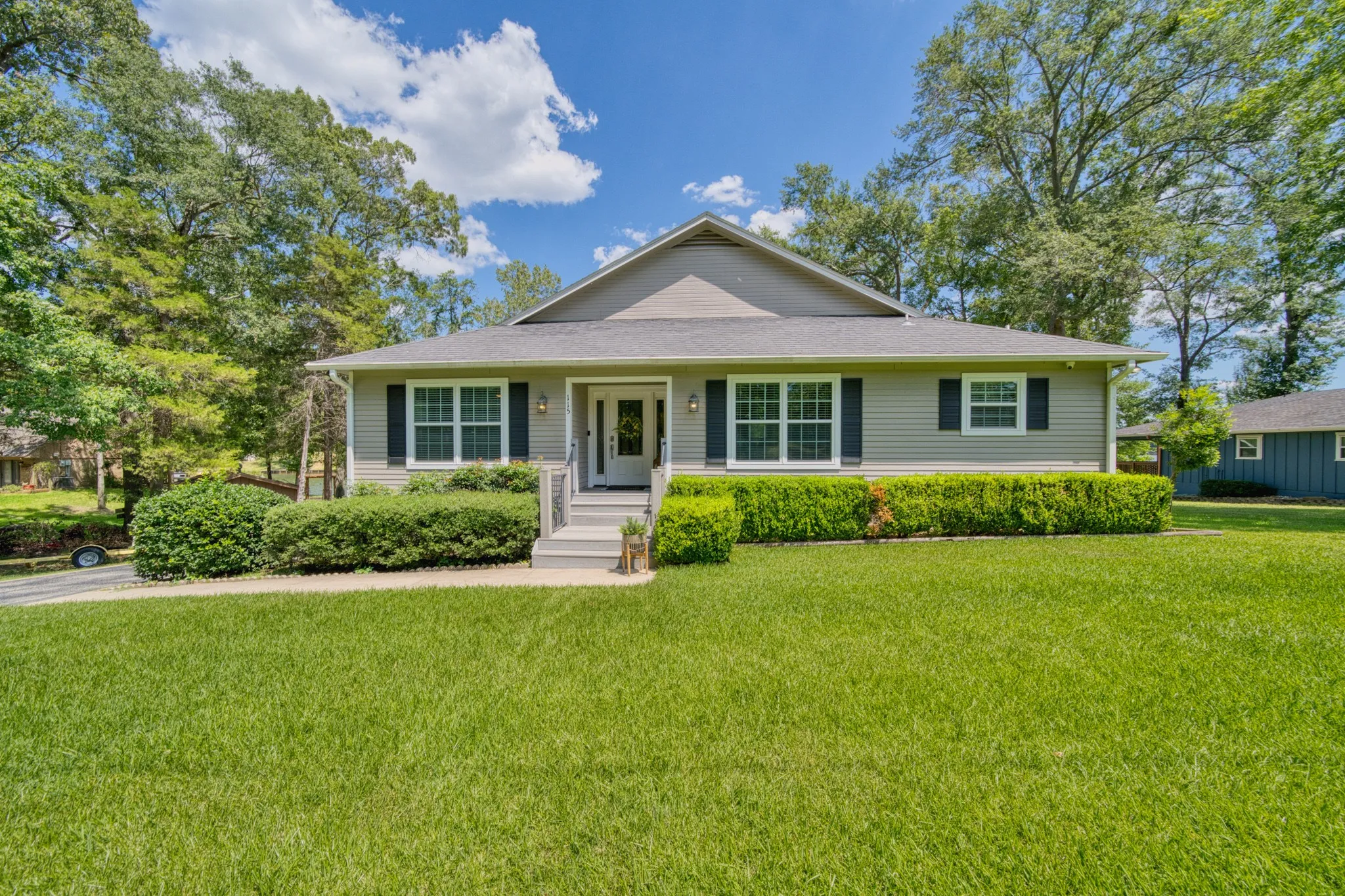 Siding exterior with contrasting dark shutters, front porch with railings, and established landscaping
