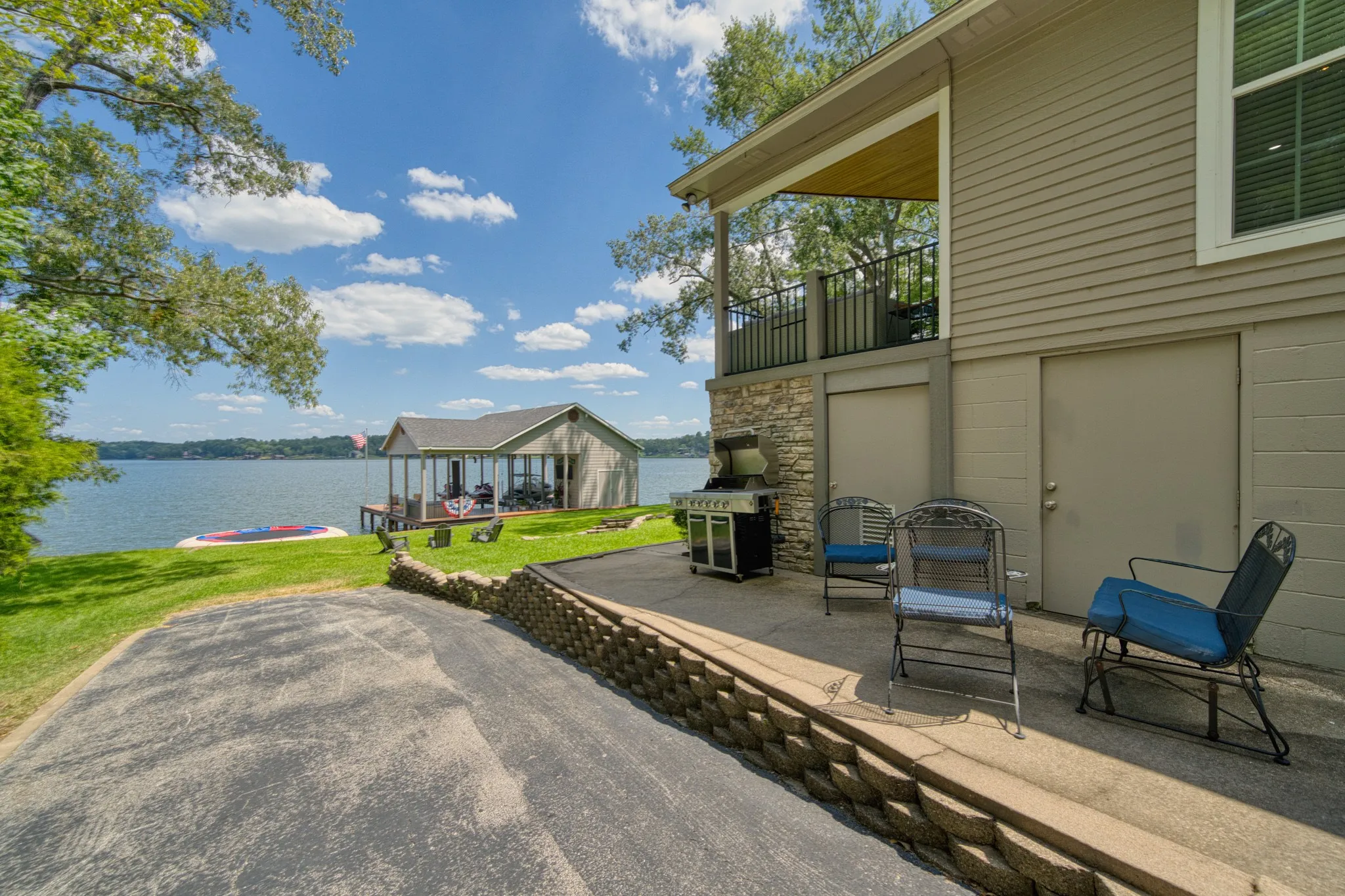 Exterior featuring a stone accent wall, an upper-level balcony with metal railing, and a lower-level patio