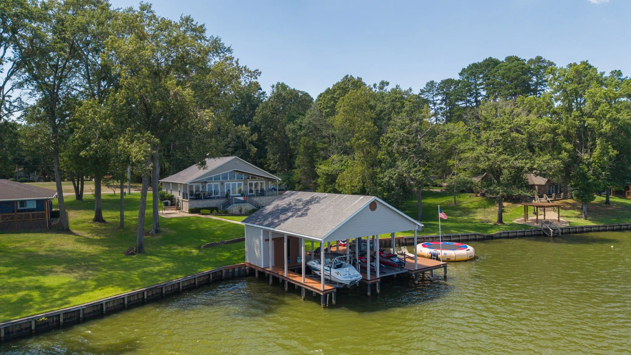 Waterfront property featuring a private boat dock with covered slips, an expansive green lawn, and a multi-level deck