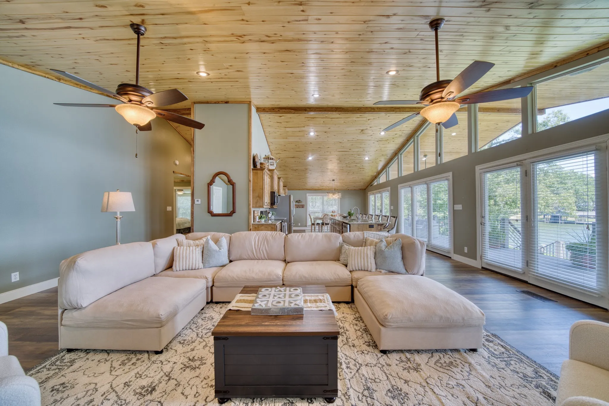 Vaulted wood-paneled ceiling with exposed beams, multiple ceiling fans with integrated lighting, expansive glass sliding doors, transom windows, and wood-finish flooring