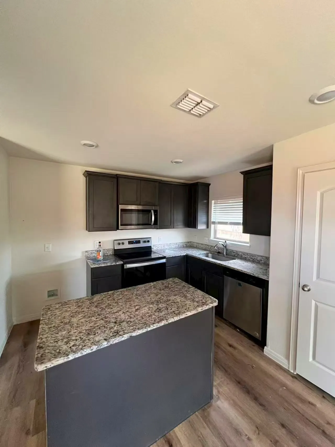 Kitchen featuring a central island, dark wood-finish cabinetry, light speckled countertops, stainless steel appliances, and wood-finish flooring