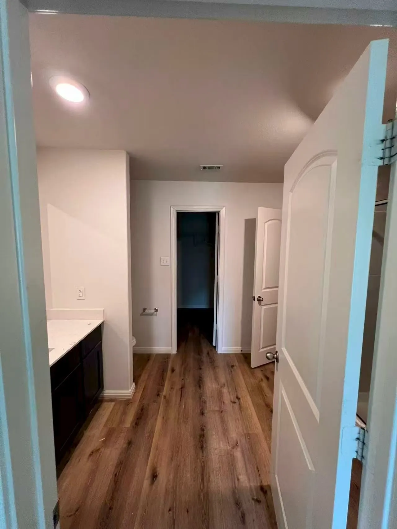 Wood-finish flooring throughout, recessed ceiling lighting, a dark wood-finish vanity with a light-colored countertop, and interior doors with arched paneling