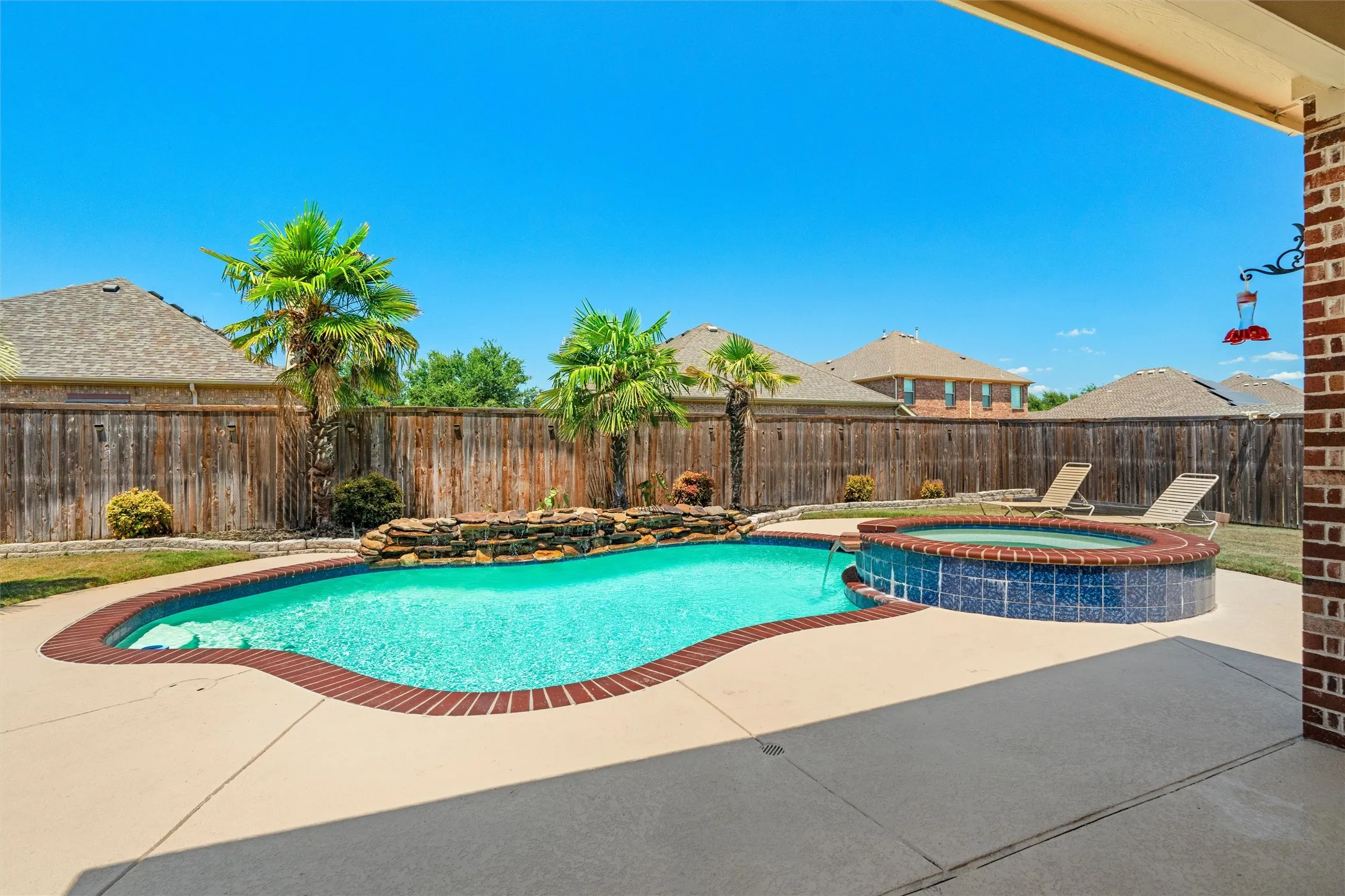 Resort-style backyard oasis featuring a lagoon-shaped saltwater pool with integrated spa, surrounded by expansive concrete decking and mature palm landscaping